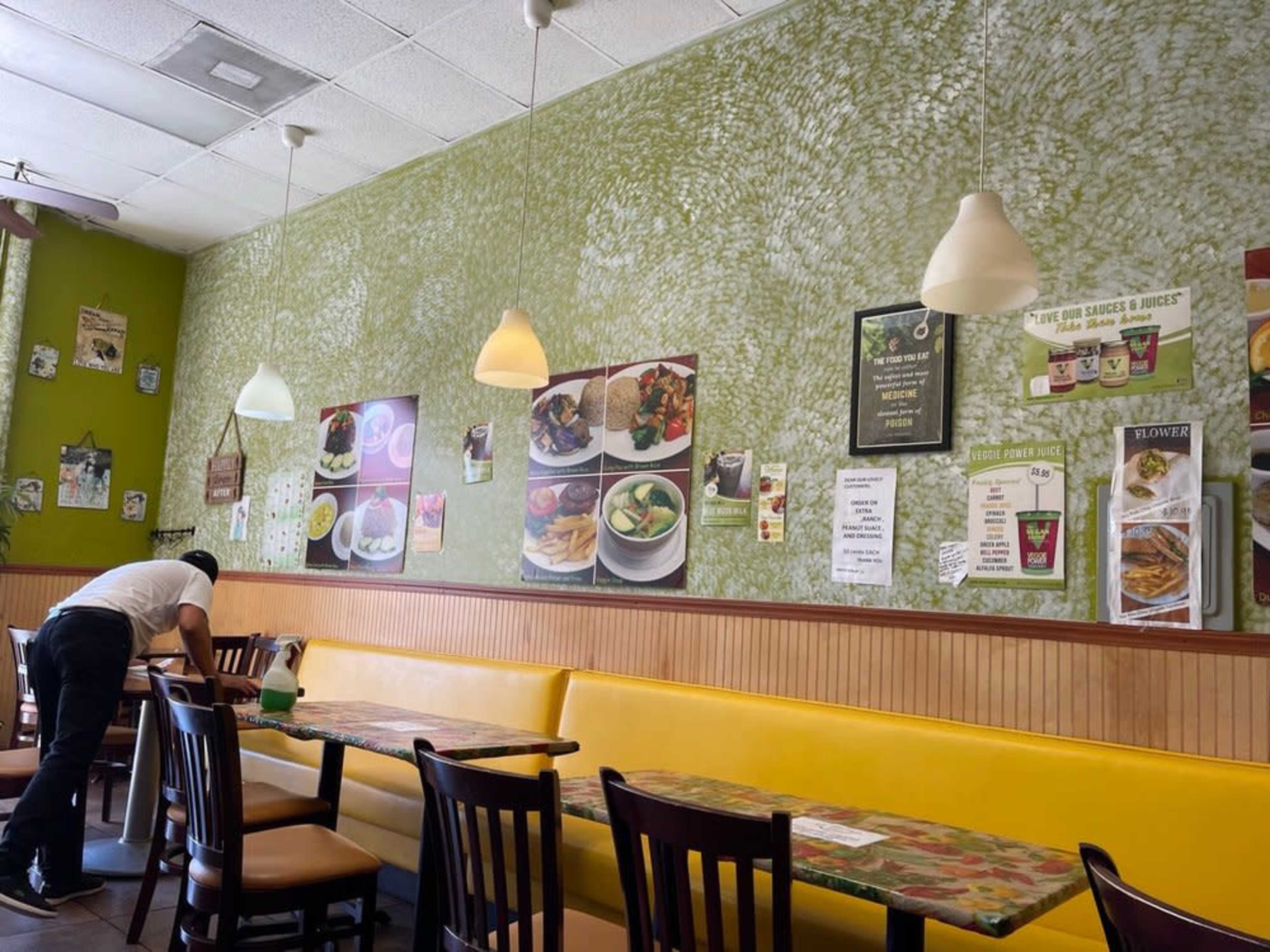 The interior of a casual restaurant features green walls, yellow seating, and various food-related posters.