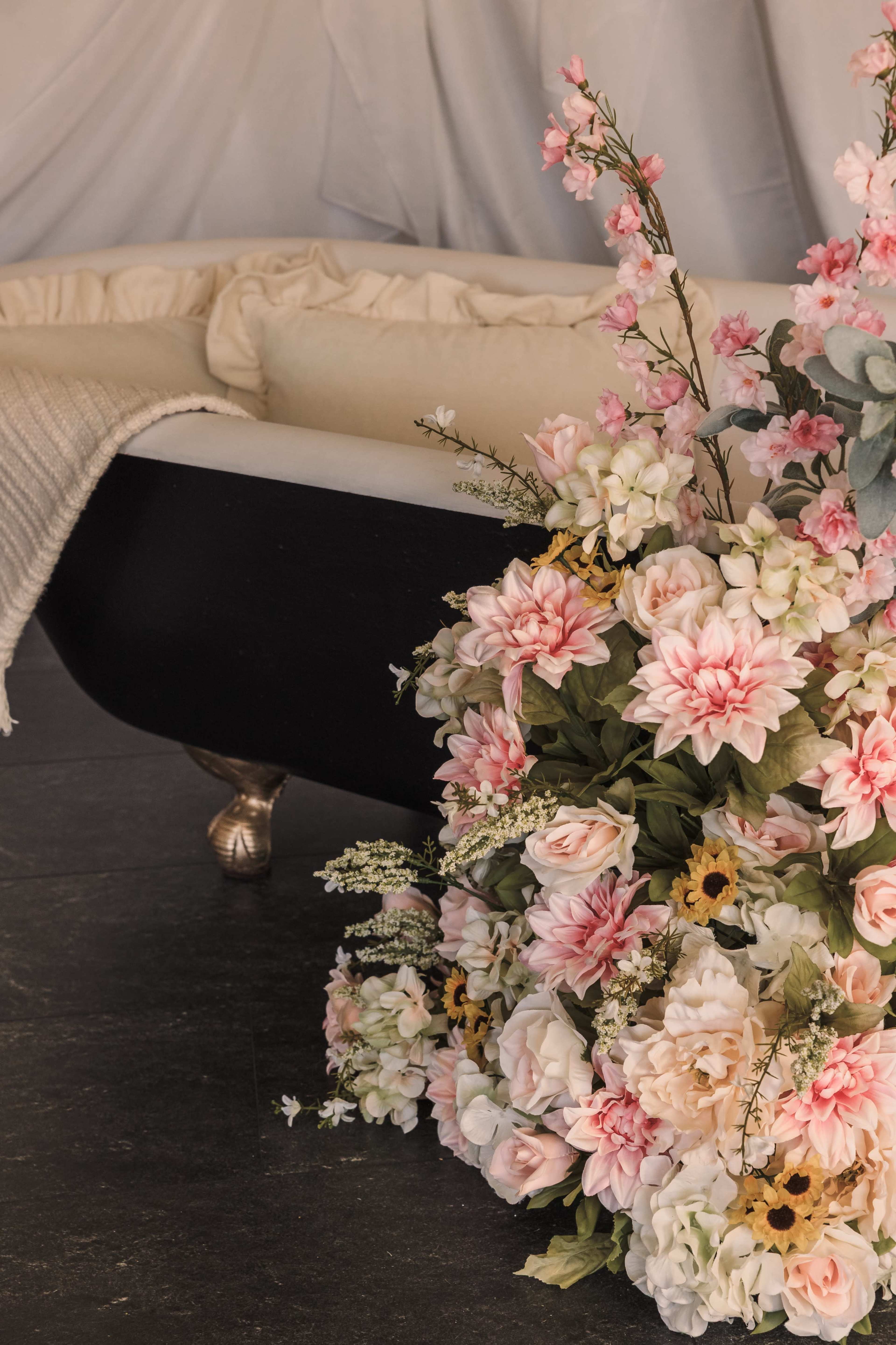 A black and white clawfoot bathtub is adorned with a large arrangement of pink and white artificial flowers positioned beside it.
