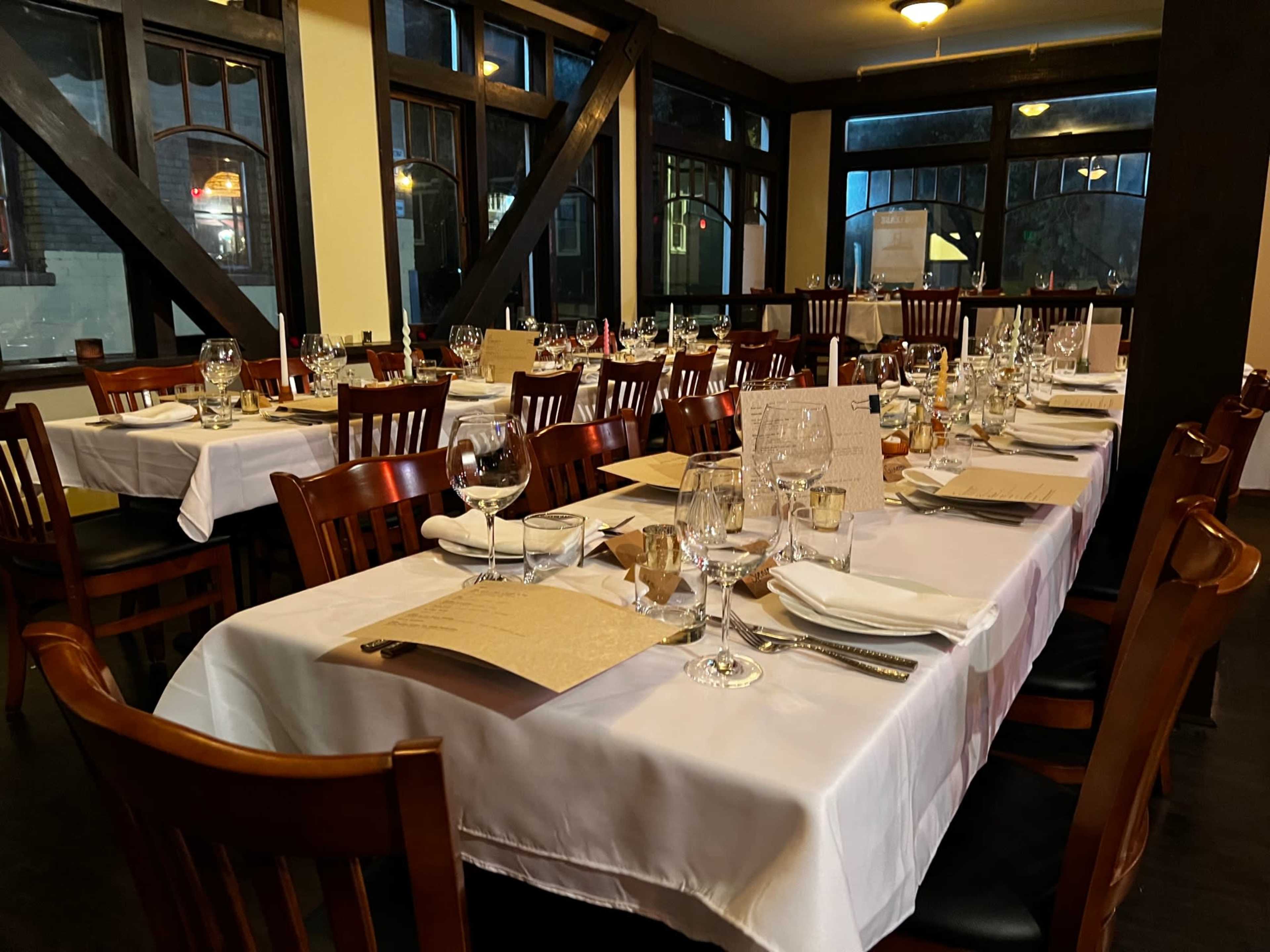 A row of neatly set tables with white tablecloths and tableware is arranged in a well-lit restaurant dining area.