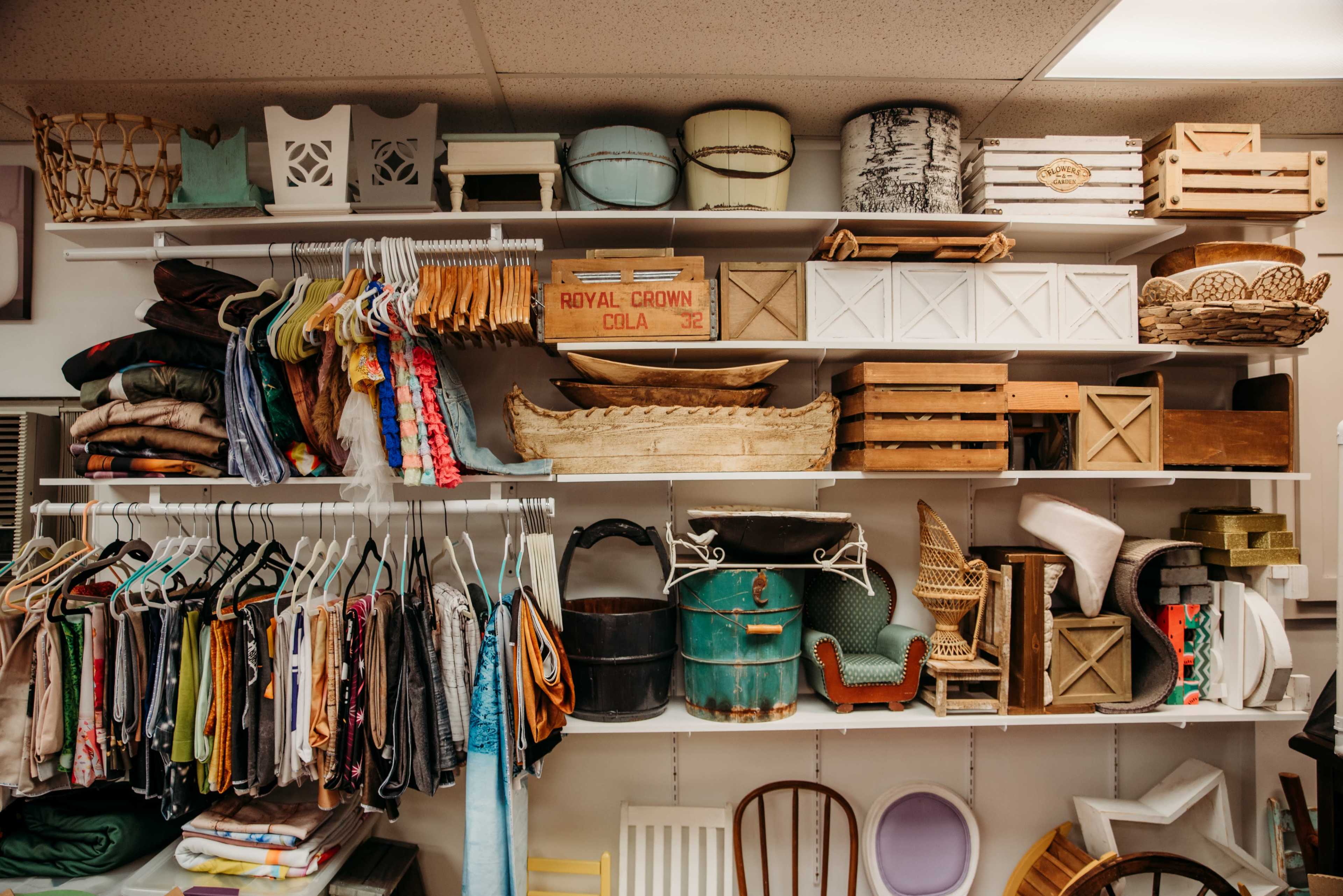 A neatly organized shelf filled with various containers, baskets, and a colorful assortment of hanging clothing.