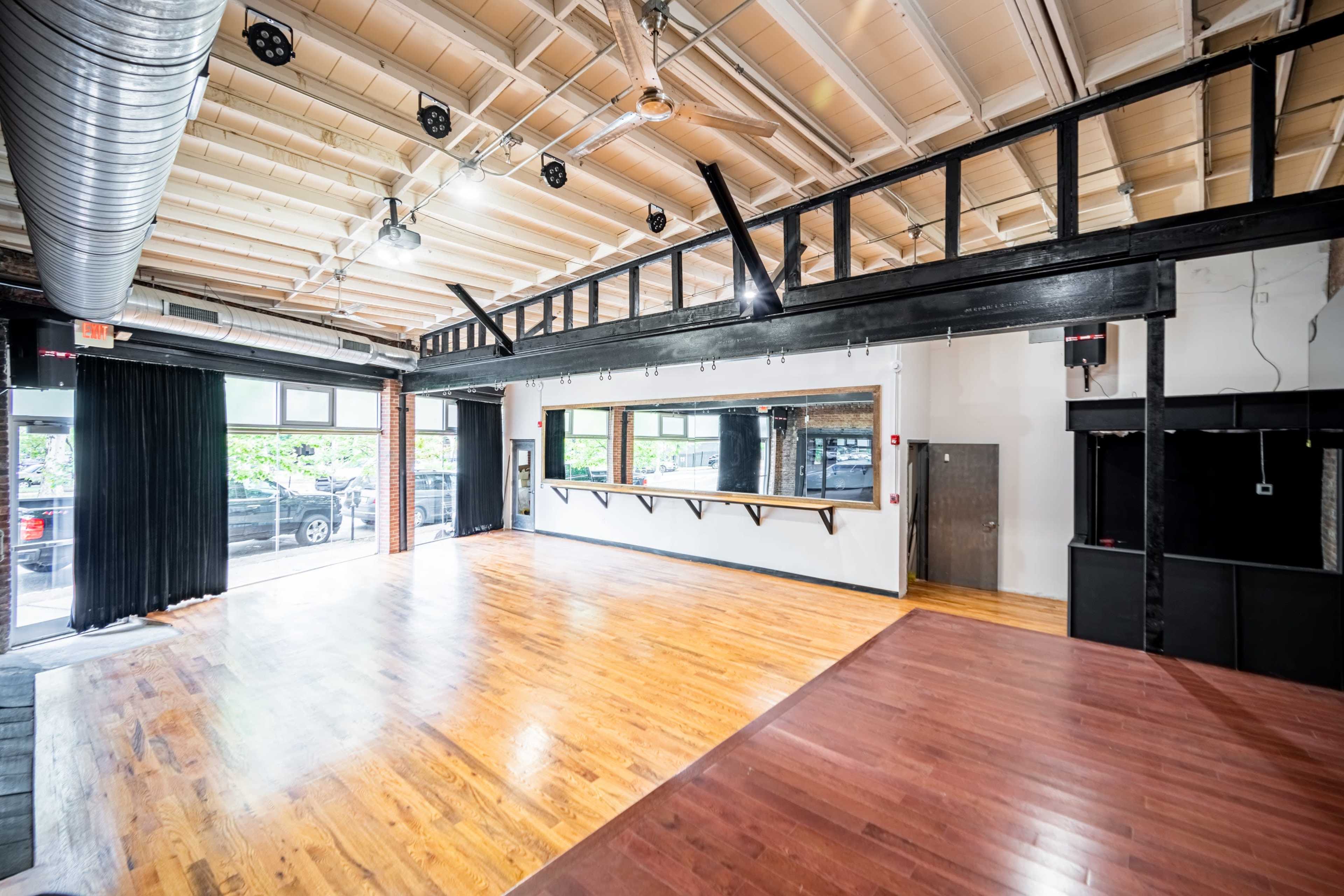 An empty, spacious interior of a room with wooden floors, large windows, and a mirror along one wall.