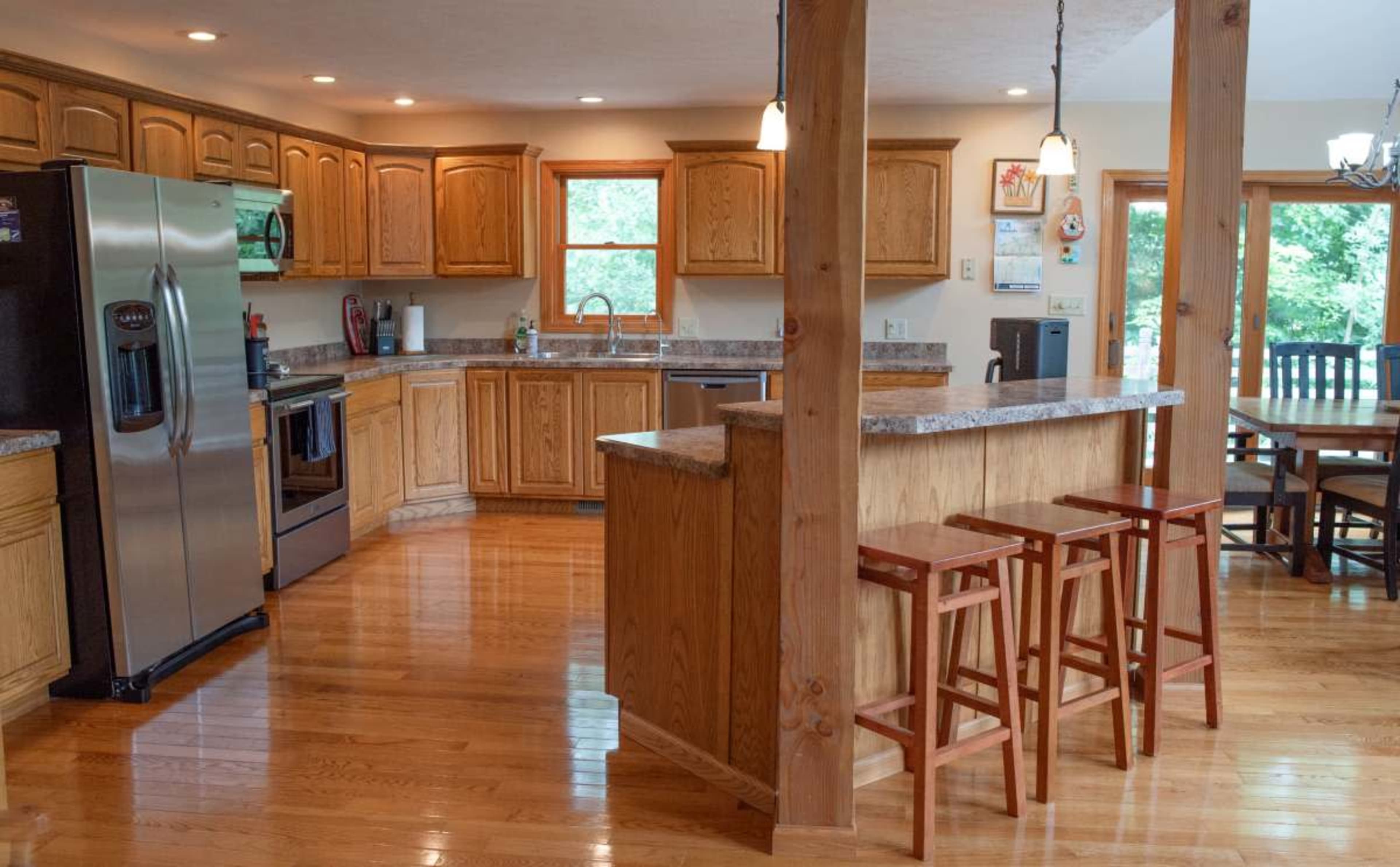 The image shows a spacious kitchen featuring wooden cabinets, stainless steel appliances, and a dining area with a table and chairs.