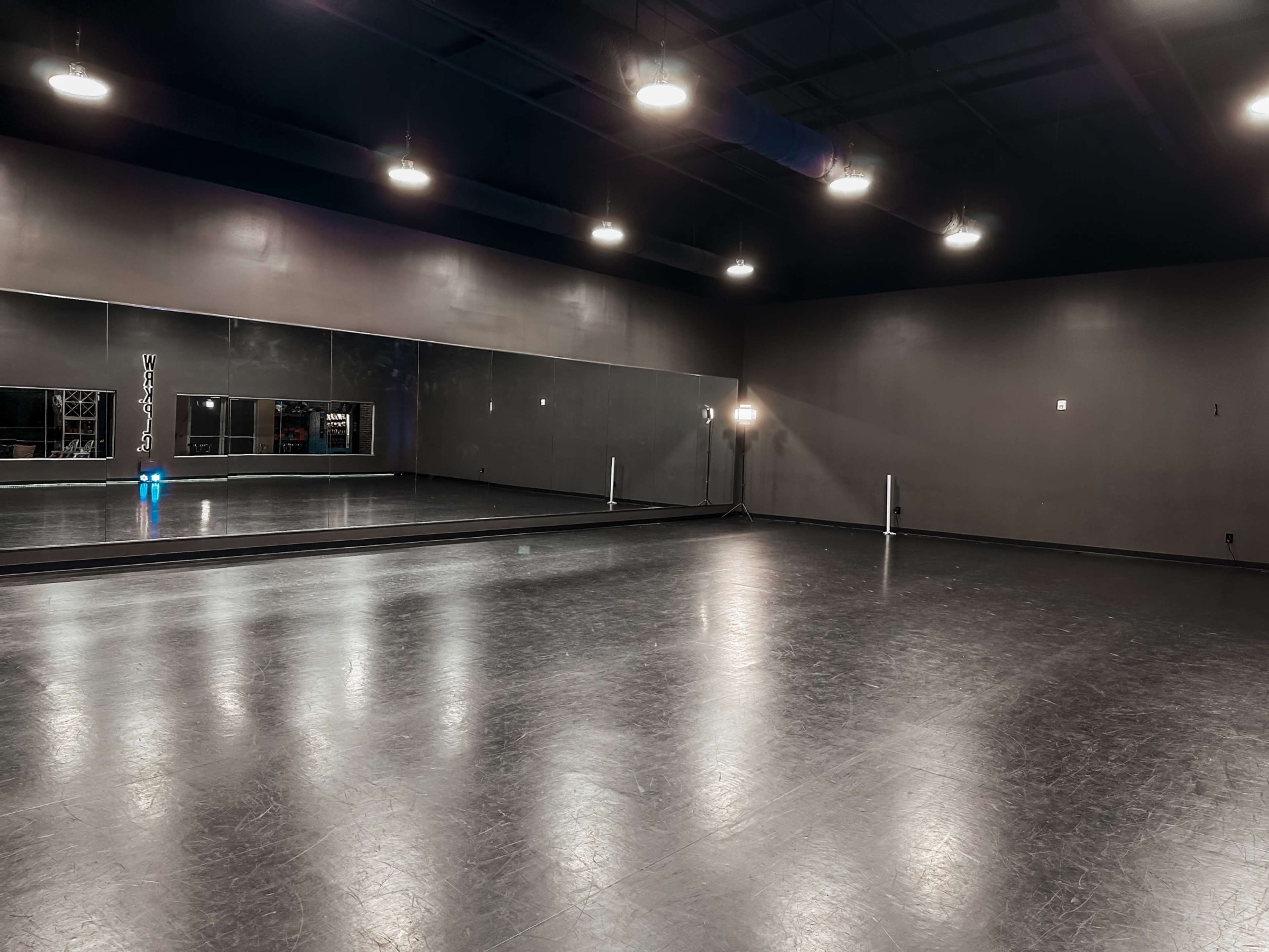 The image shows an empty dance studio with dark walls, a large mirrored wall, and overhead lighting.