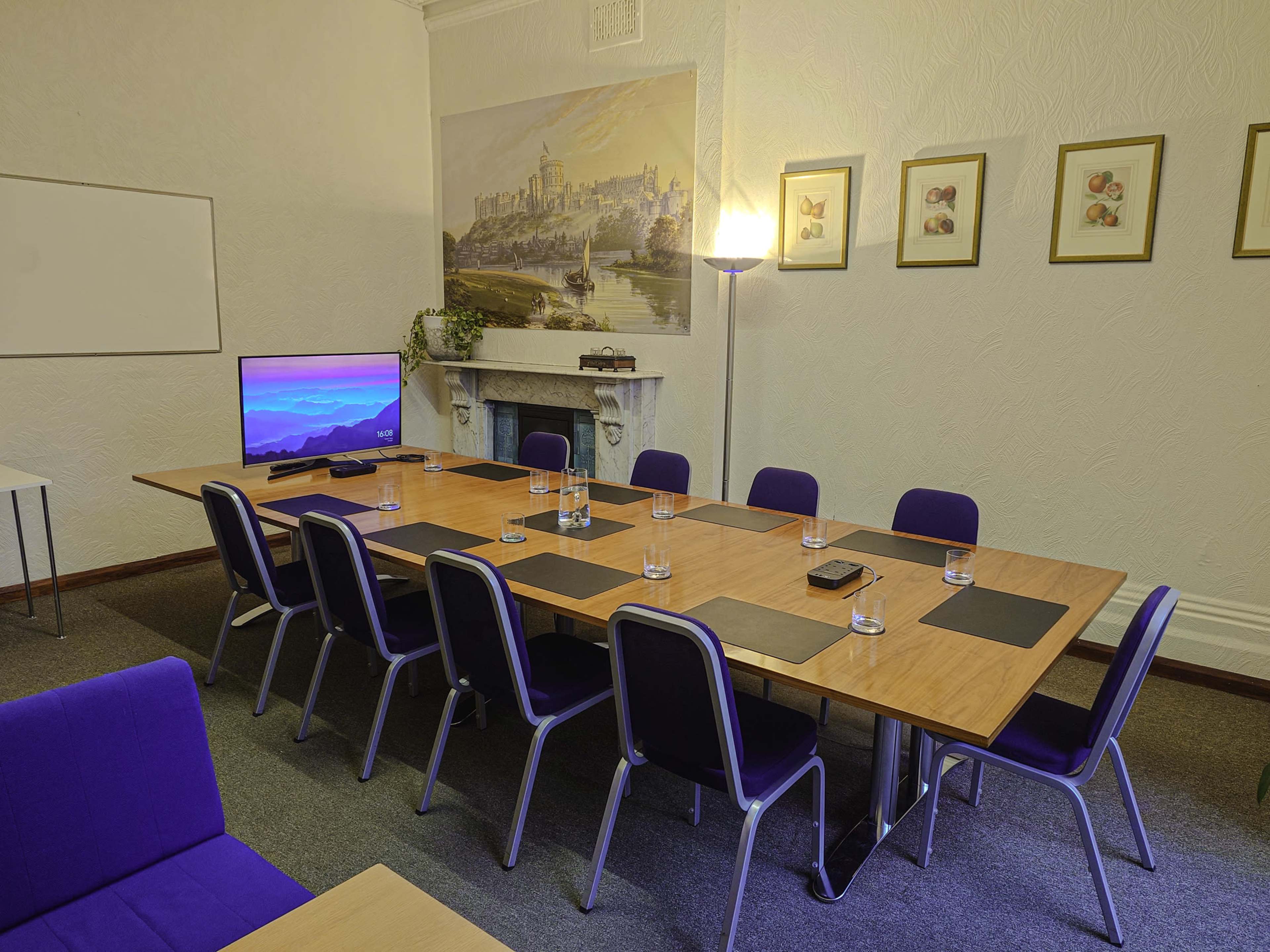 A large conference room features a long rectangular table with chairs, a television mounted on a wall, and framed artwork.