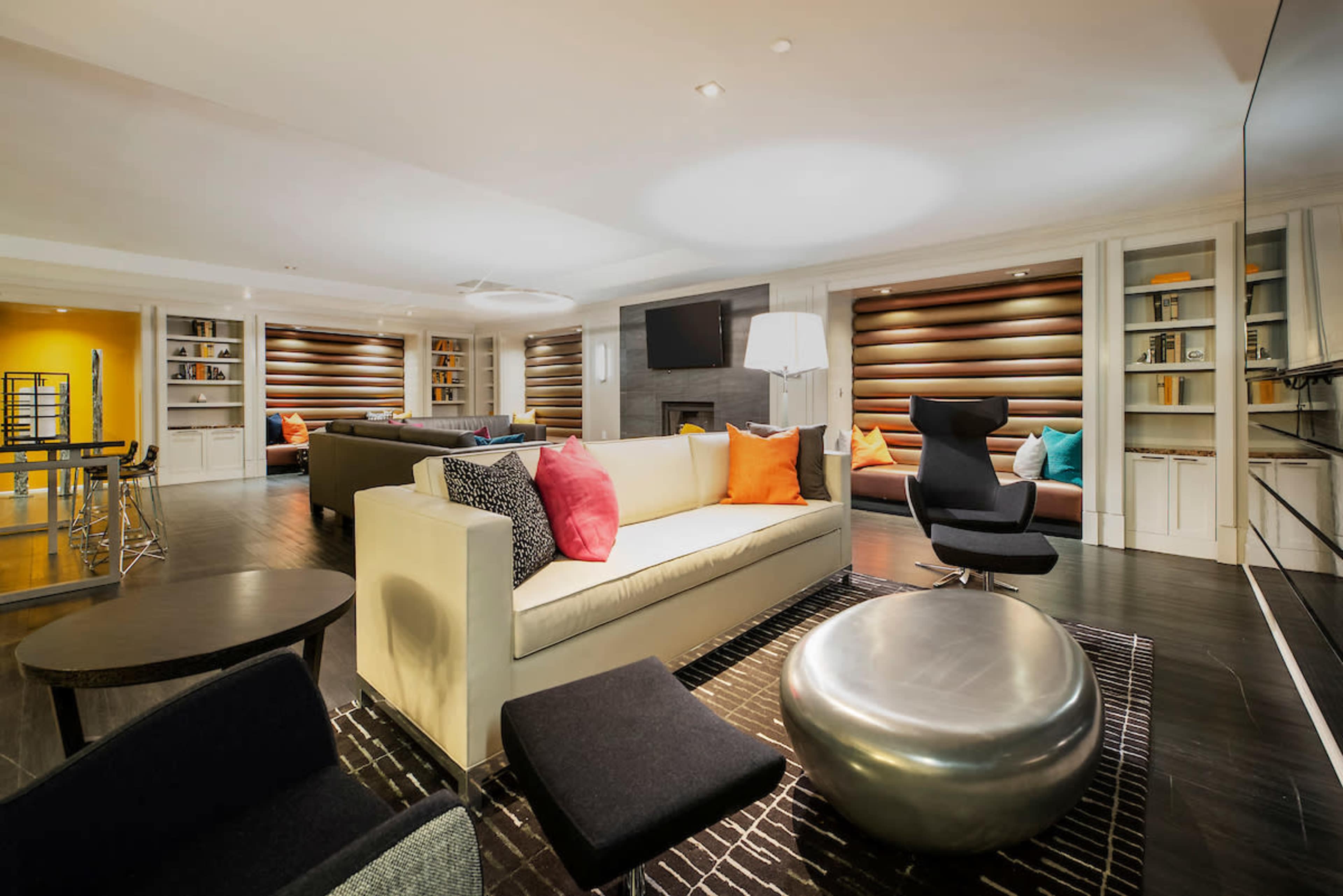A modern living room features a light-colored sofa with colorful cushions, a round metallic coffee table, and a dark rug with minimalistic chairs.