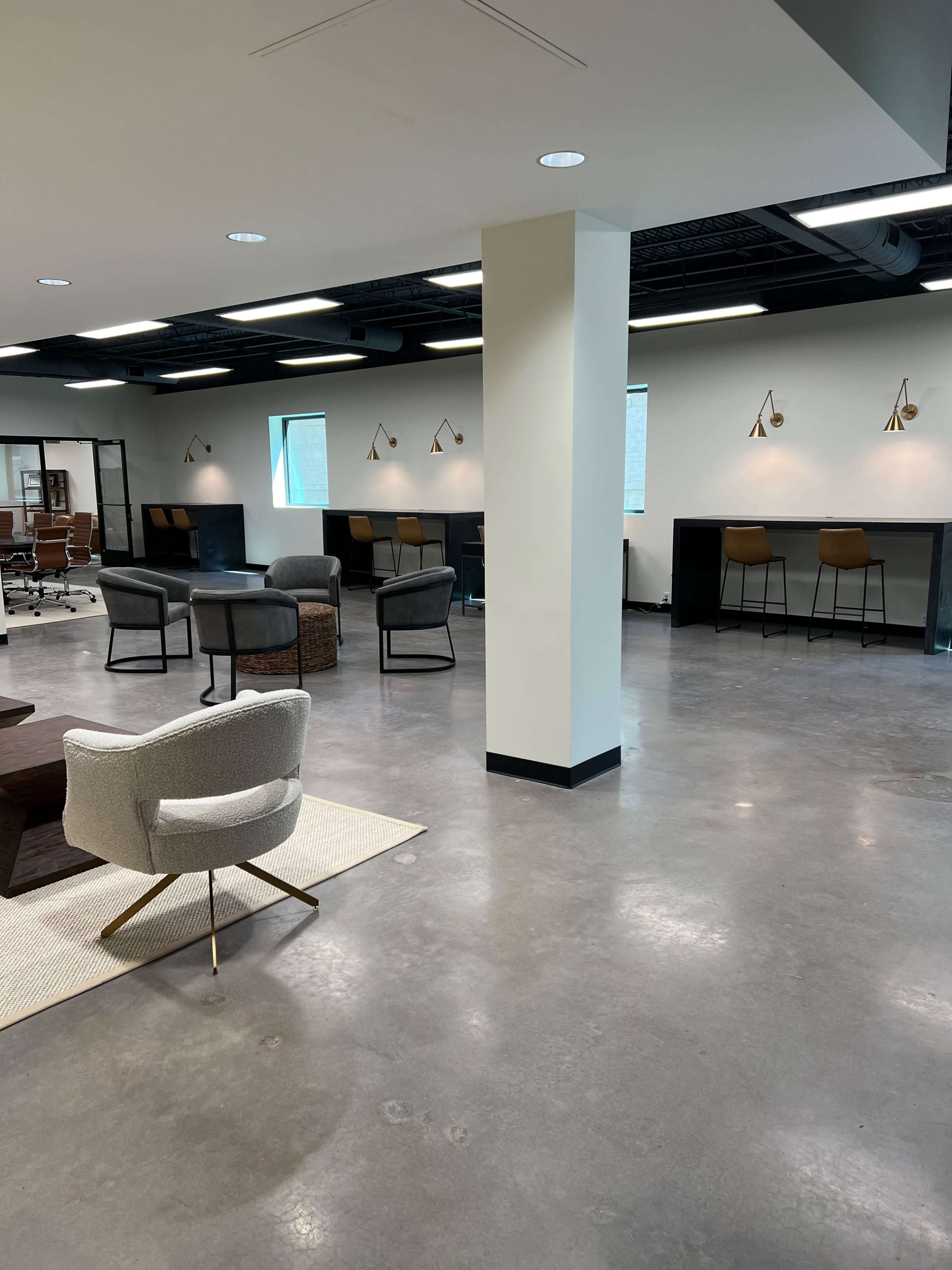 A modern office space with various seating arrangements, including chairs and barstools, and a polished concrete floor.