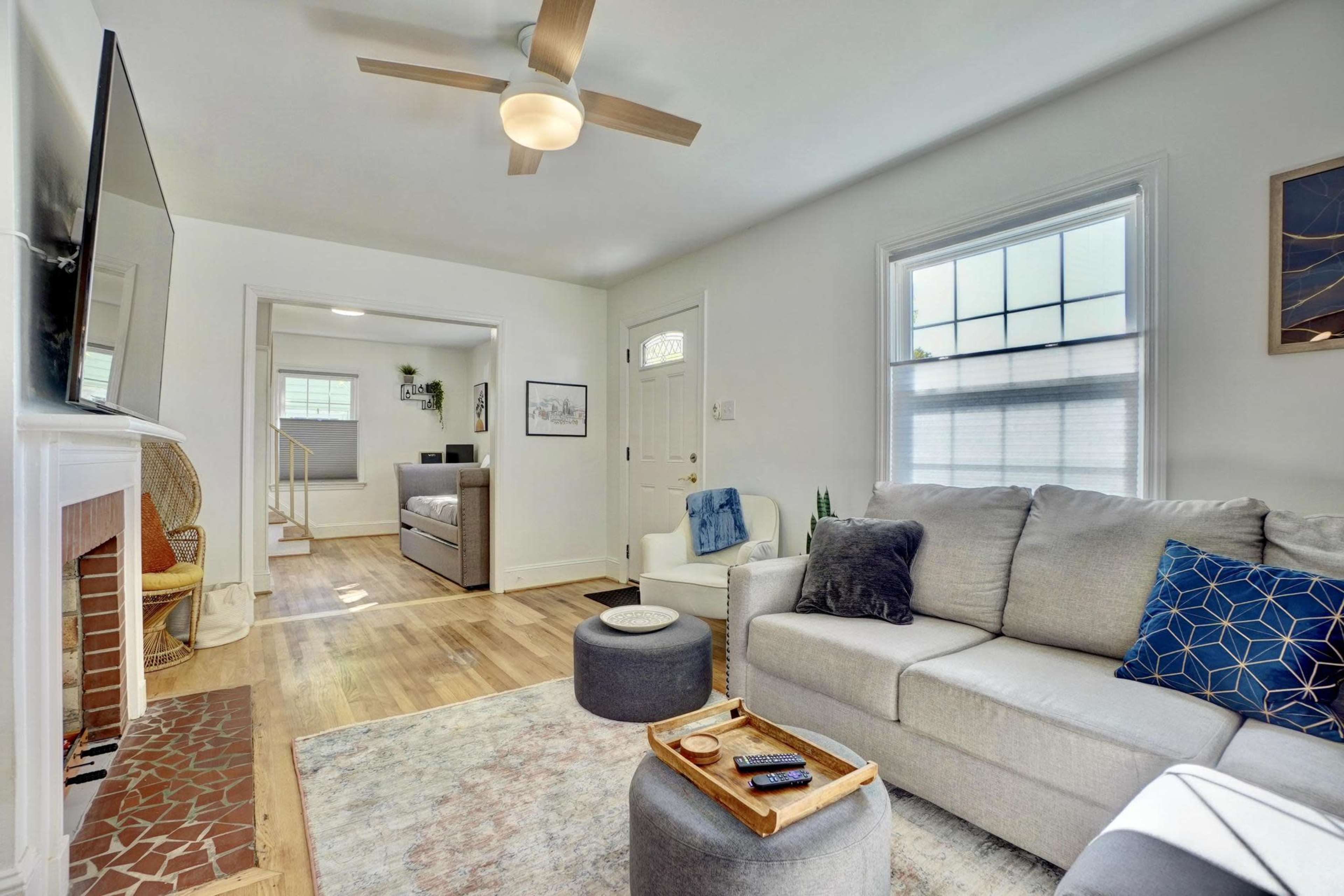 The image depicts a well-lit living room with a gray sectional sofa, a wooden coffee table, a ceiling fan, and a doorway leading to another room.