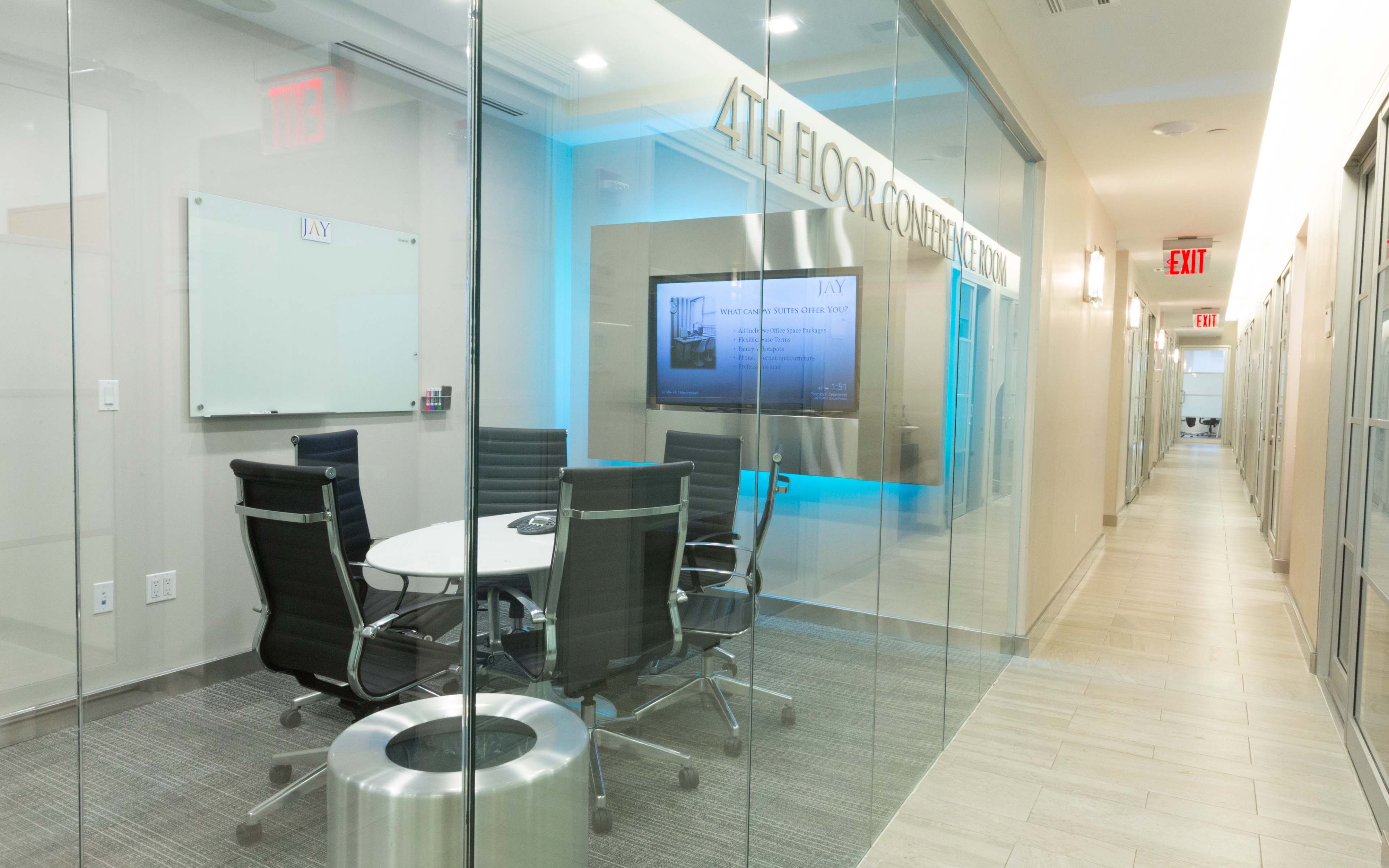 A glass-walled conference room with a round table and black chairs is located on the fourth floor, illuminated by blue lighting.