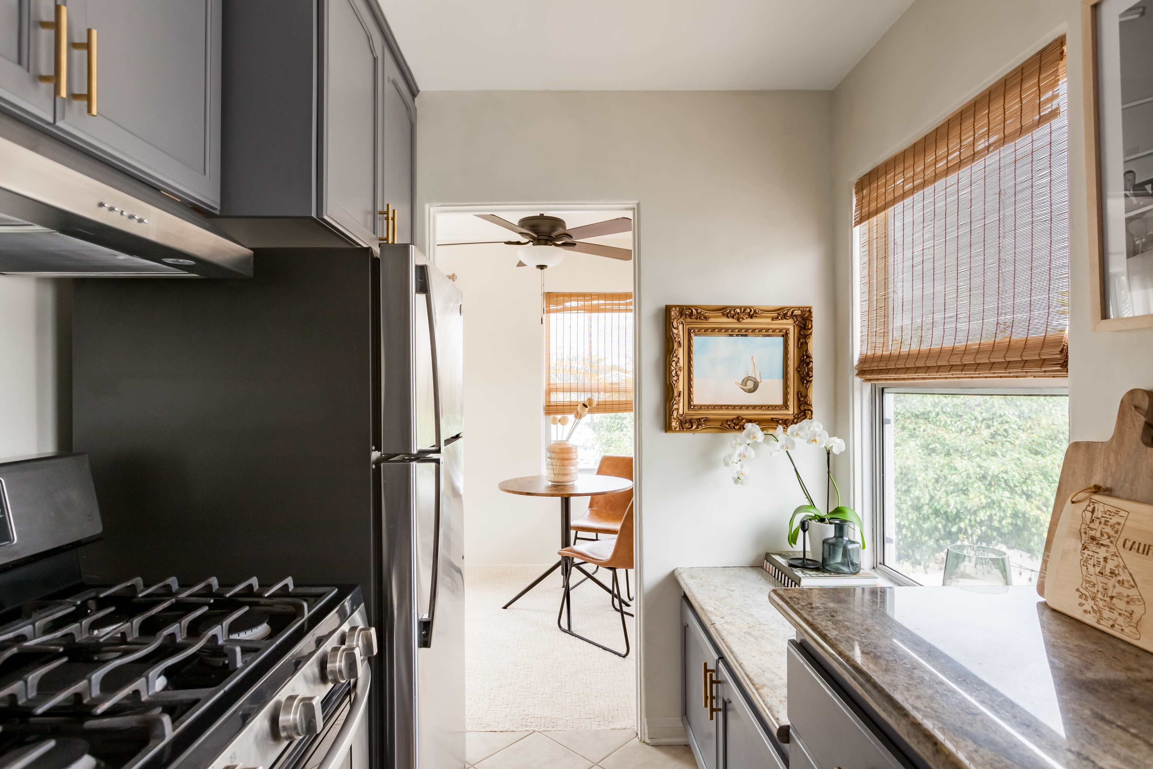 A modern kitchen features dark cabinetry, a stainless steel stove, and a view into a dining area with natural light streaming in through the windows.