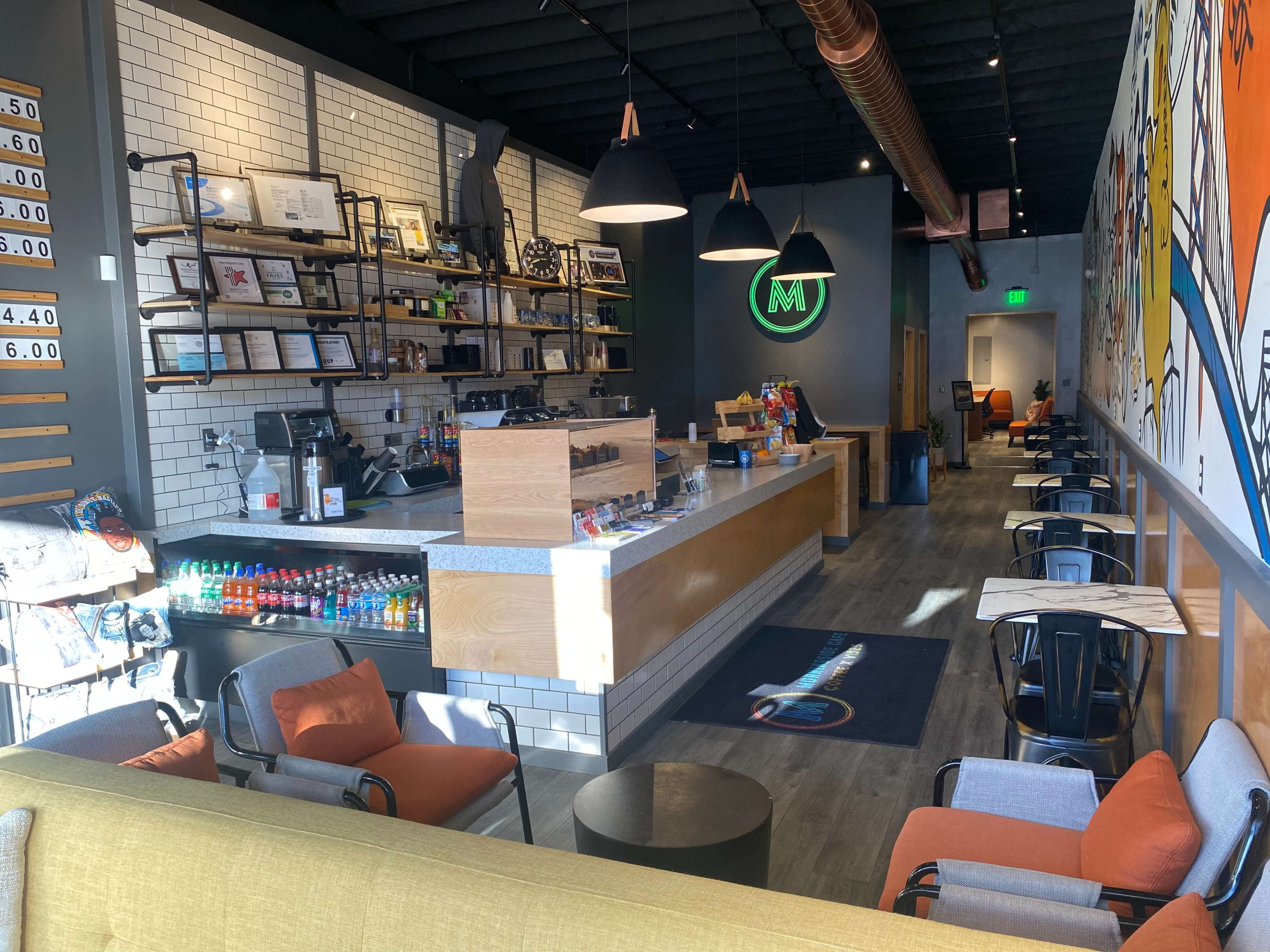 A modern café interior with a serving counter, seating areas, and a colorful mural on the wall.