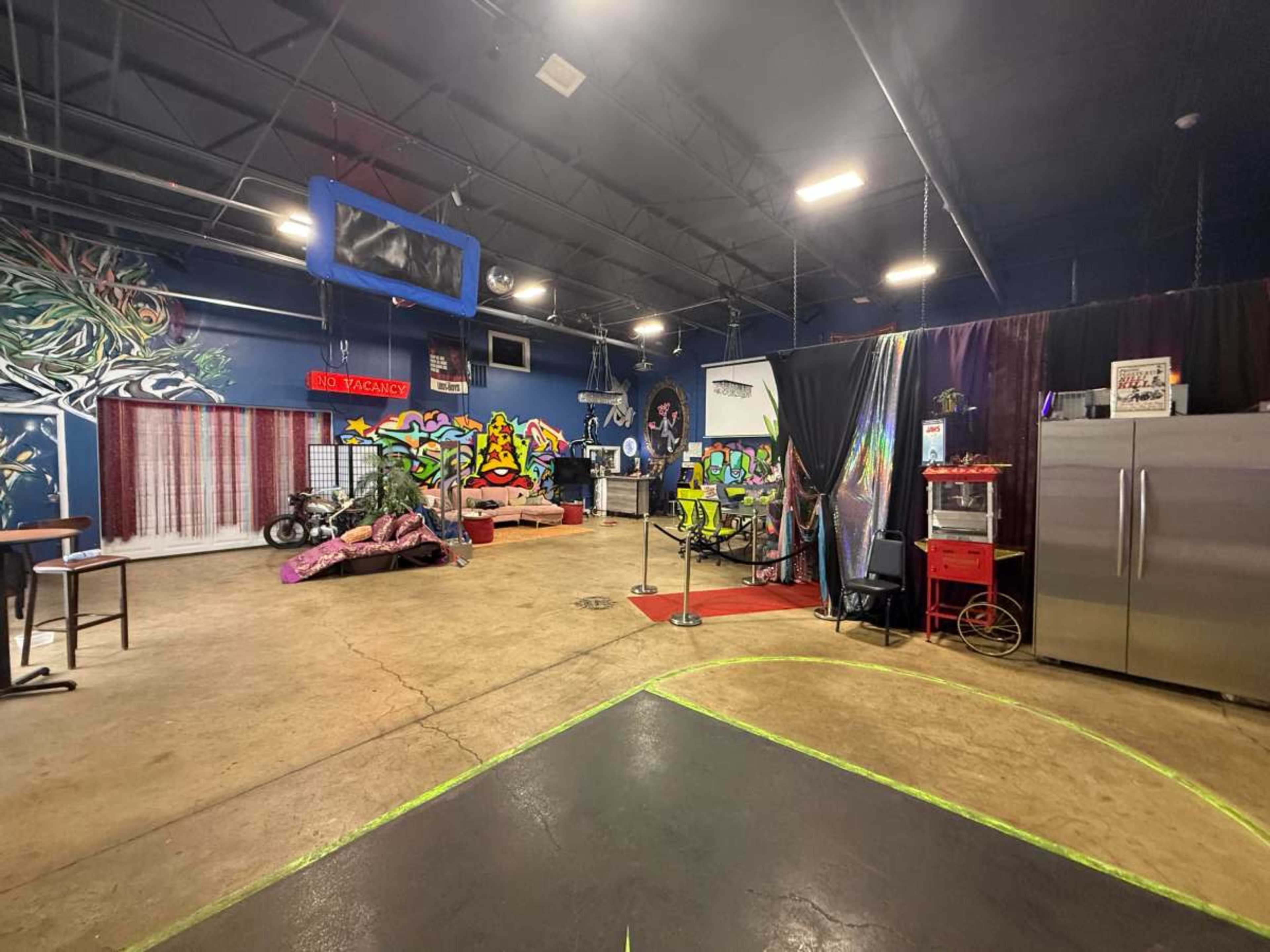 The image shows an indoor space featuring colorful graffiti on the walls, various pieces of furniture, and motorcycles on display.
