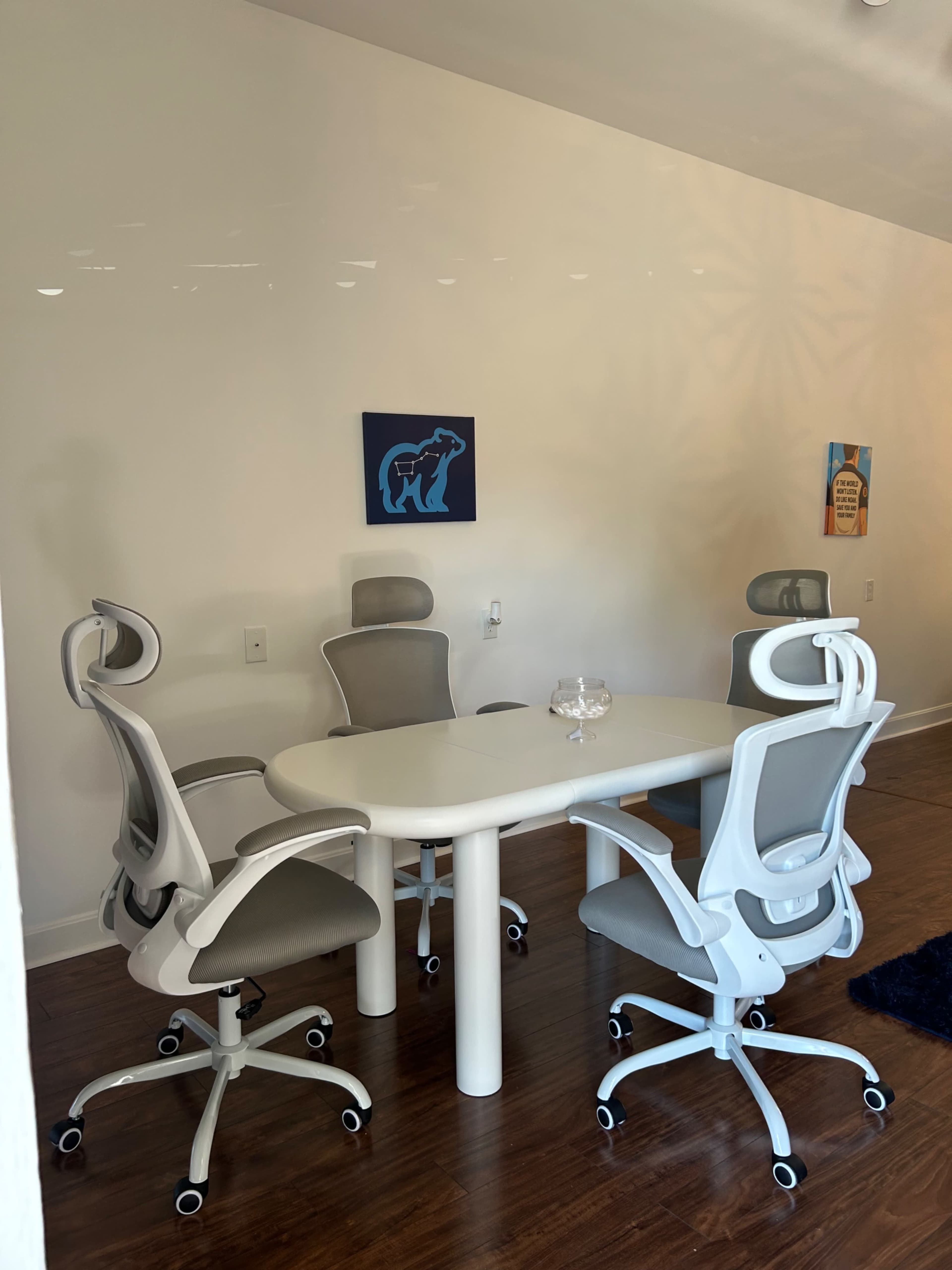 A modern meeting room features a white oval table surrounded by four ergonomic chairs.