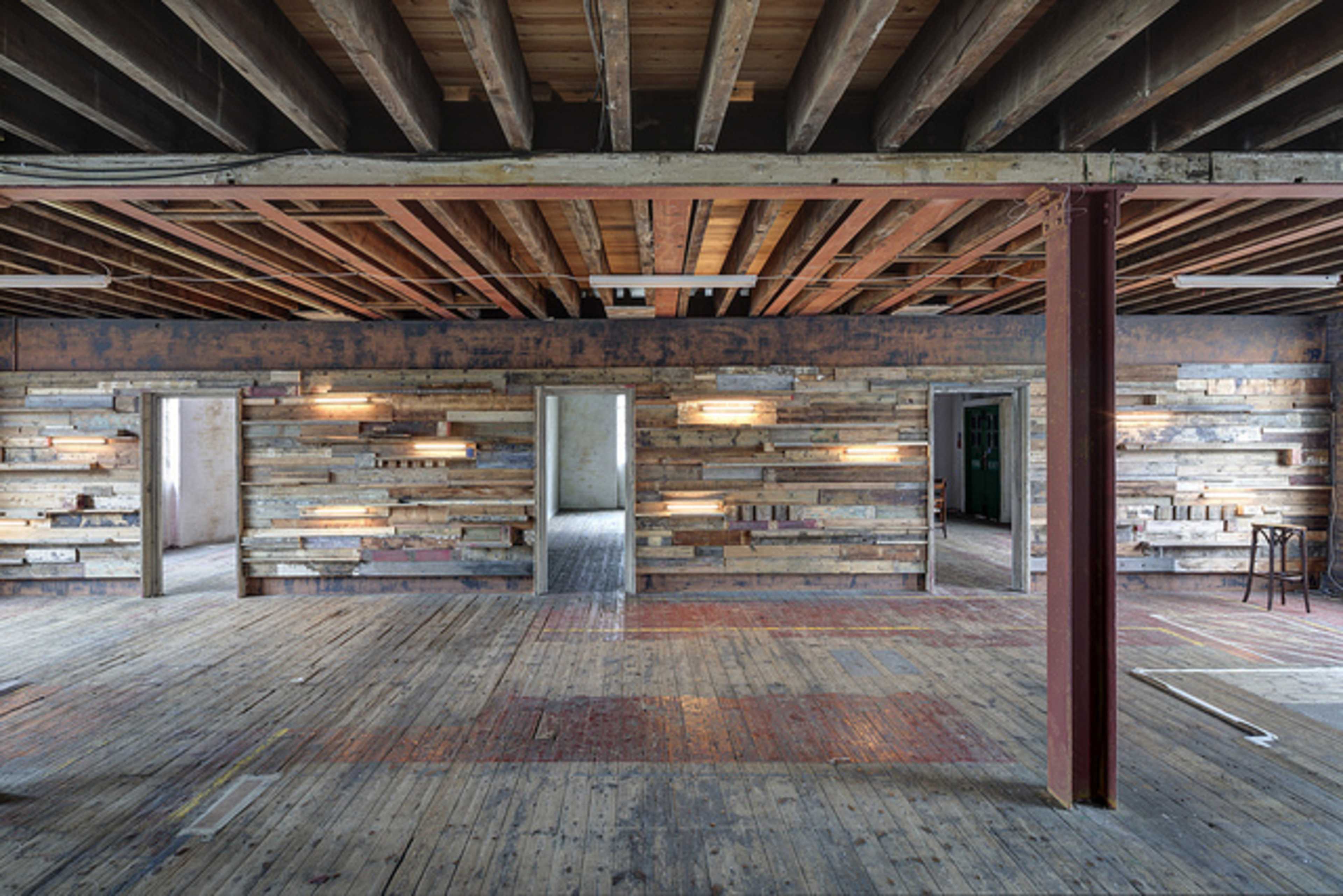 An open room with exposed wooden beams, wooden plank walls, and minimal furnishings.