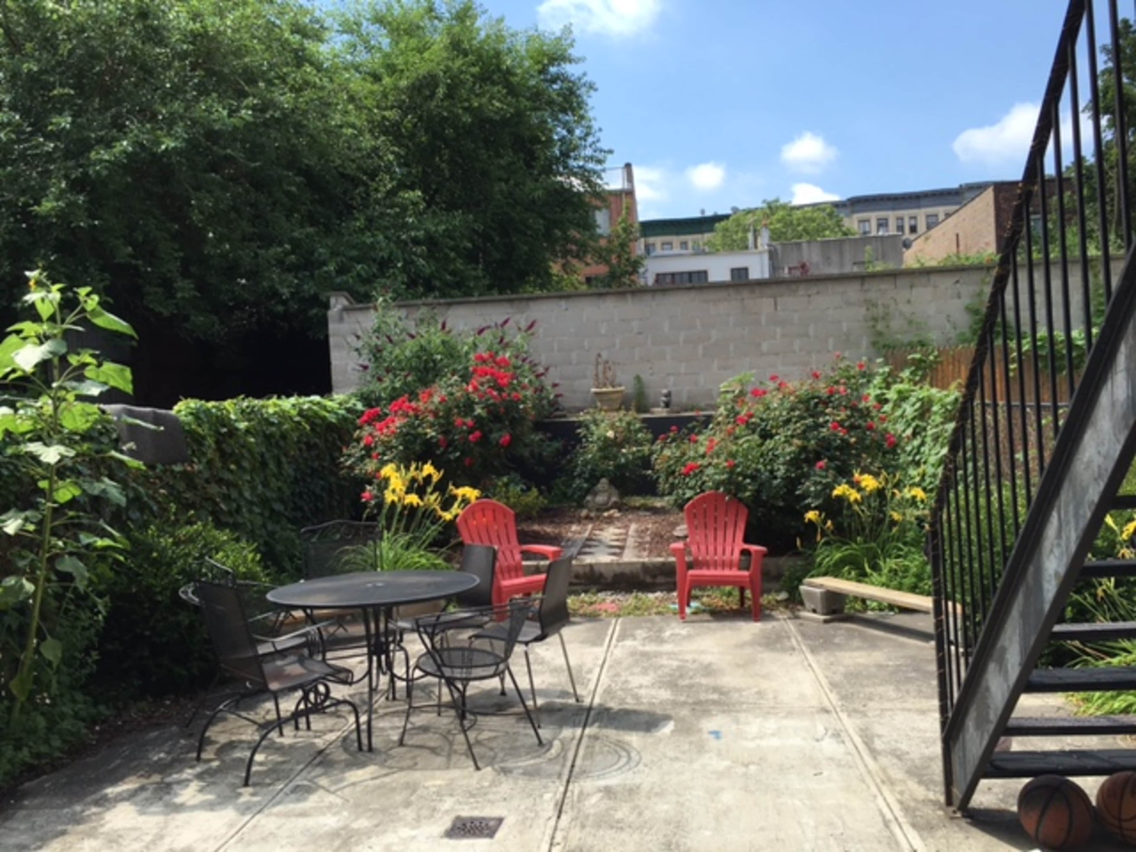 A garden space features a round black table and chairs surrounded by colorful flower beds and a stone pathway.