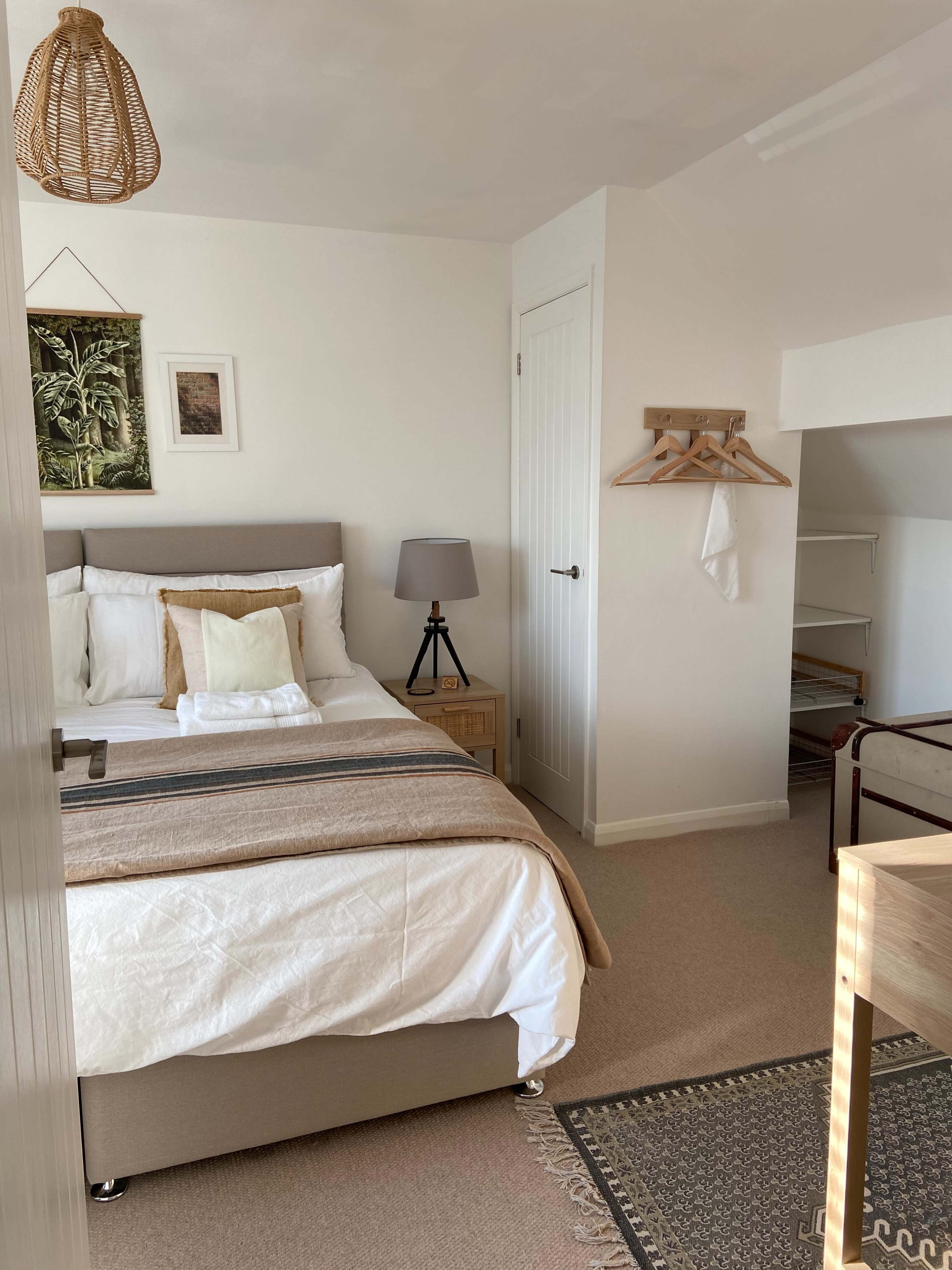 A well-decorated bedroom featuring a bed with white linens, a nightstand with a lamp, and a clothing rack against the wall.