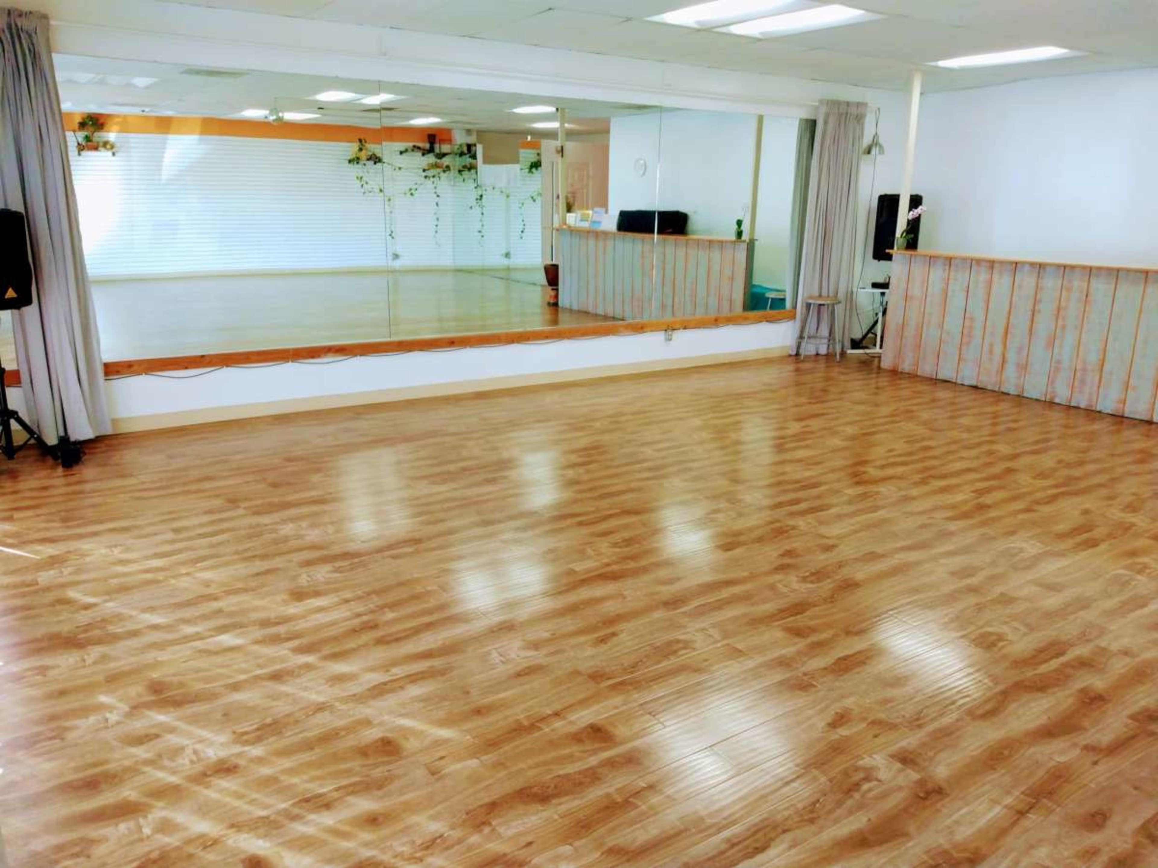 A spacious dance studio with a wooden floor, large mirrors along one wall, and soft lighting.