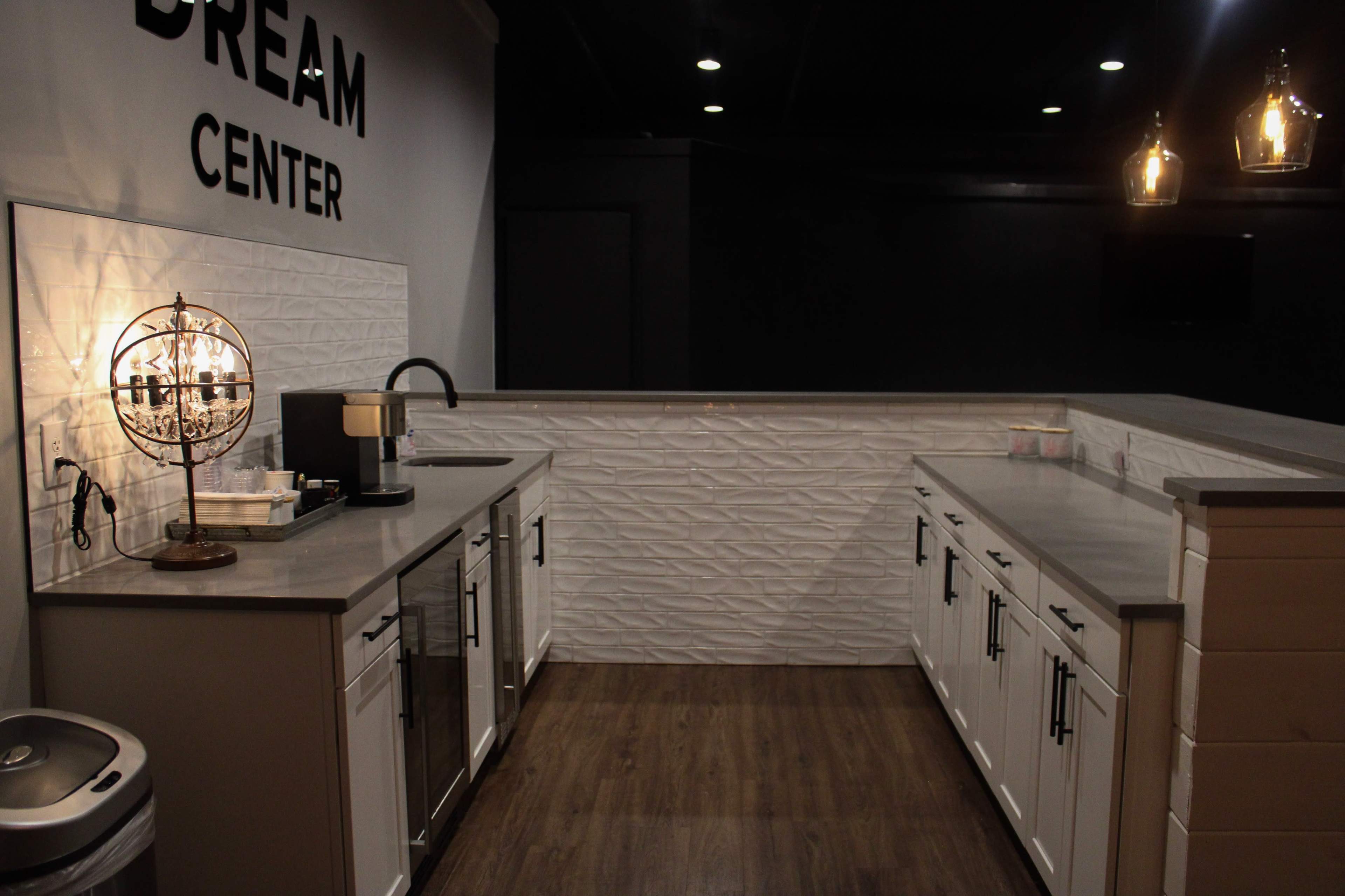 A modern kitchen space with white cabinetry, gray countertops, and a textured wall, labeled "DREAM CENTER."
