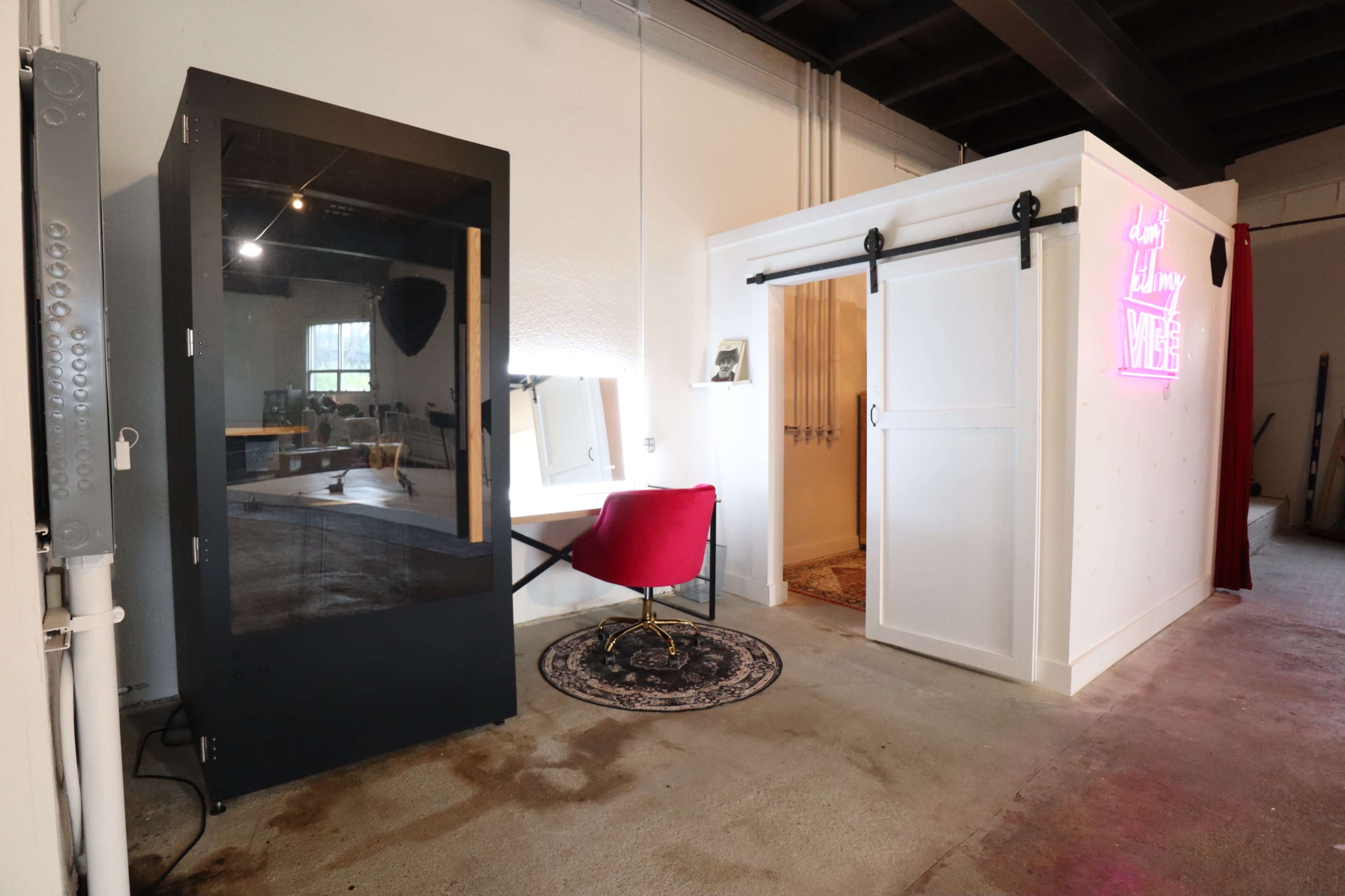 The scene features a modern workspace with a black booth on the left and a white, sliding door structure on the right, which is illuminated by a neon sign.