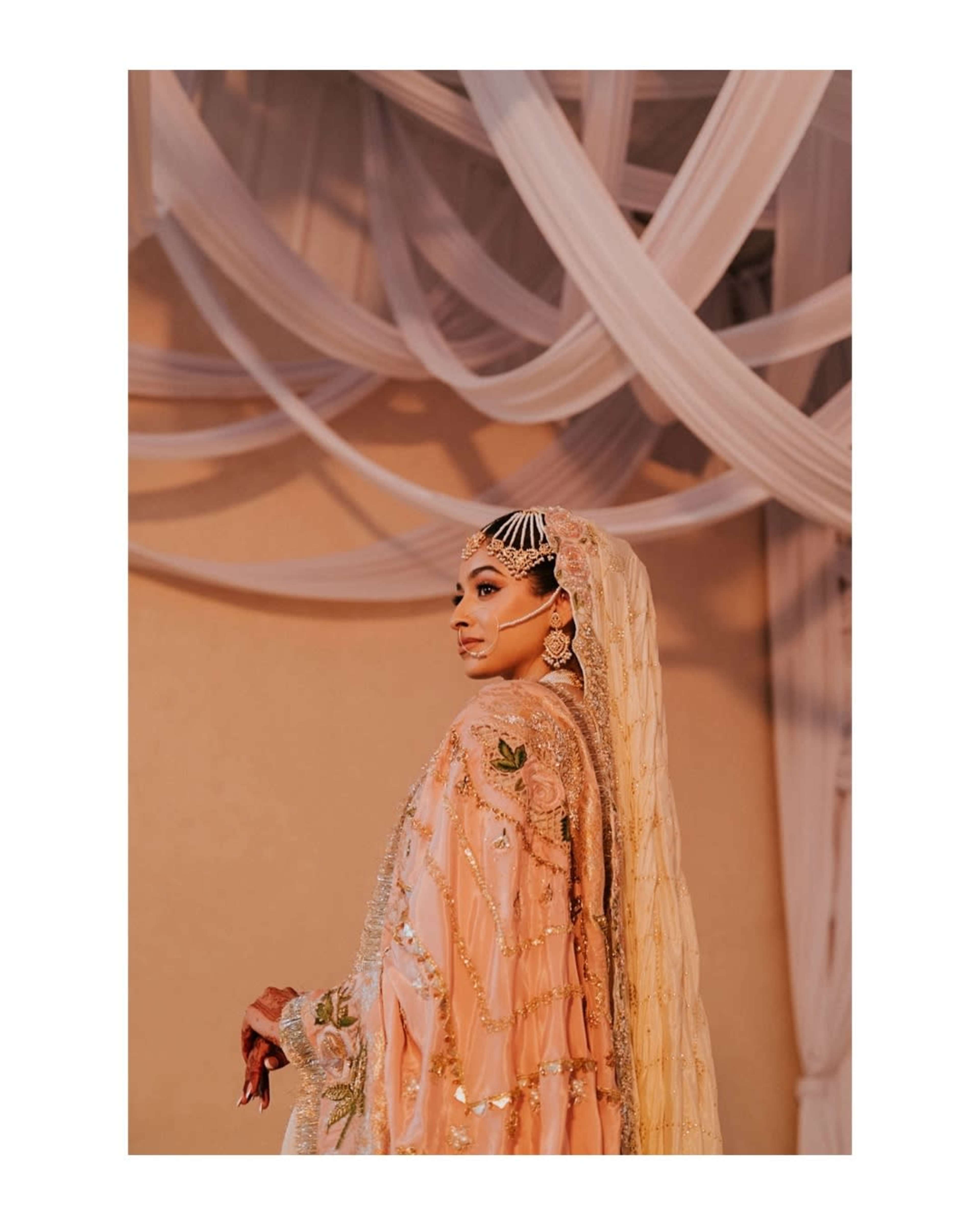 A woman in traditional attire poses against a backdrop of draped fabric.