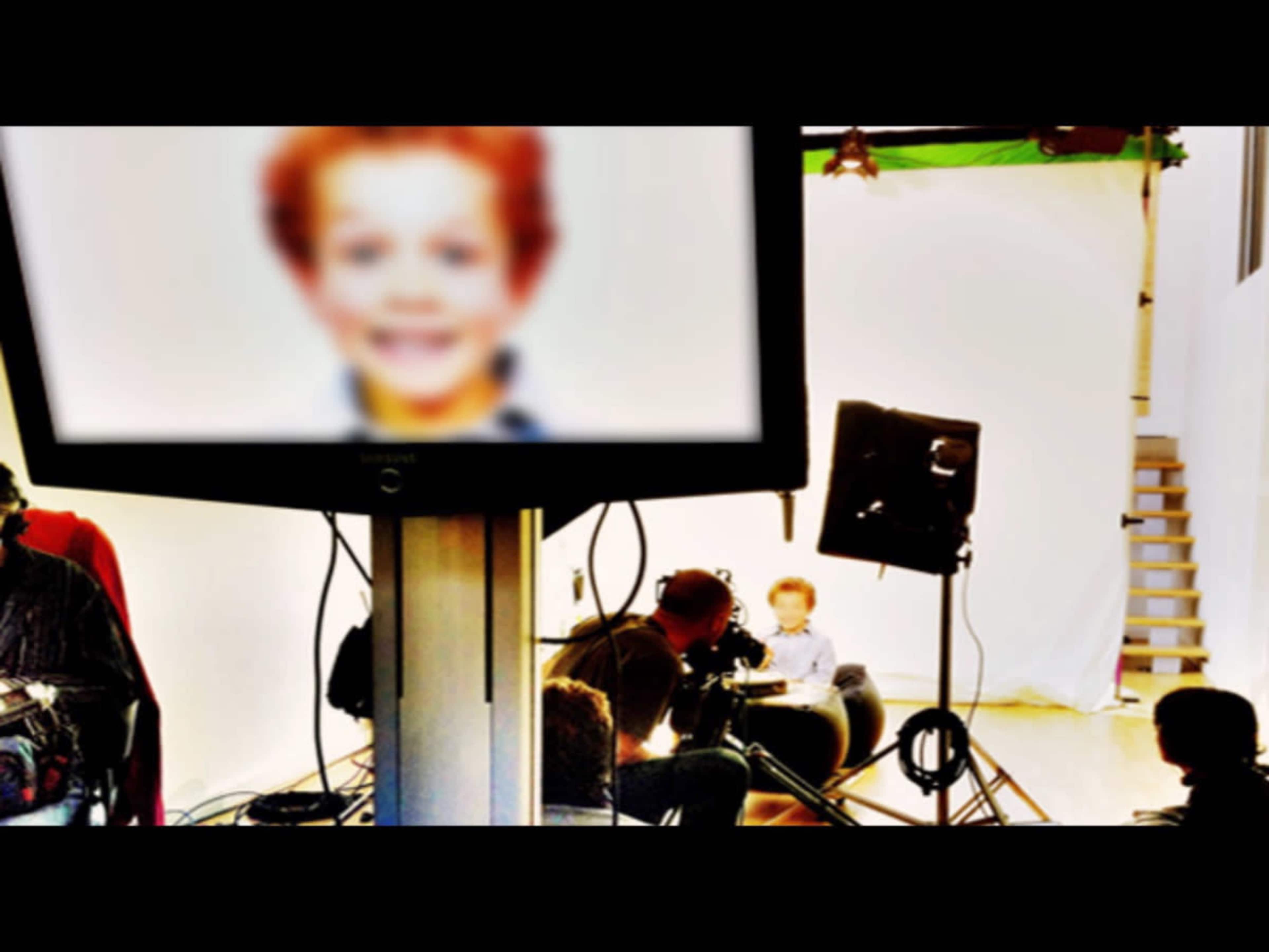A blurry image of a child is displayed on a monitor in a studio setting while a film crew prepares to shoot.