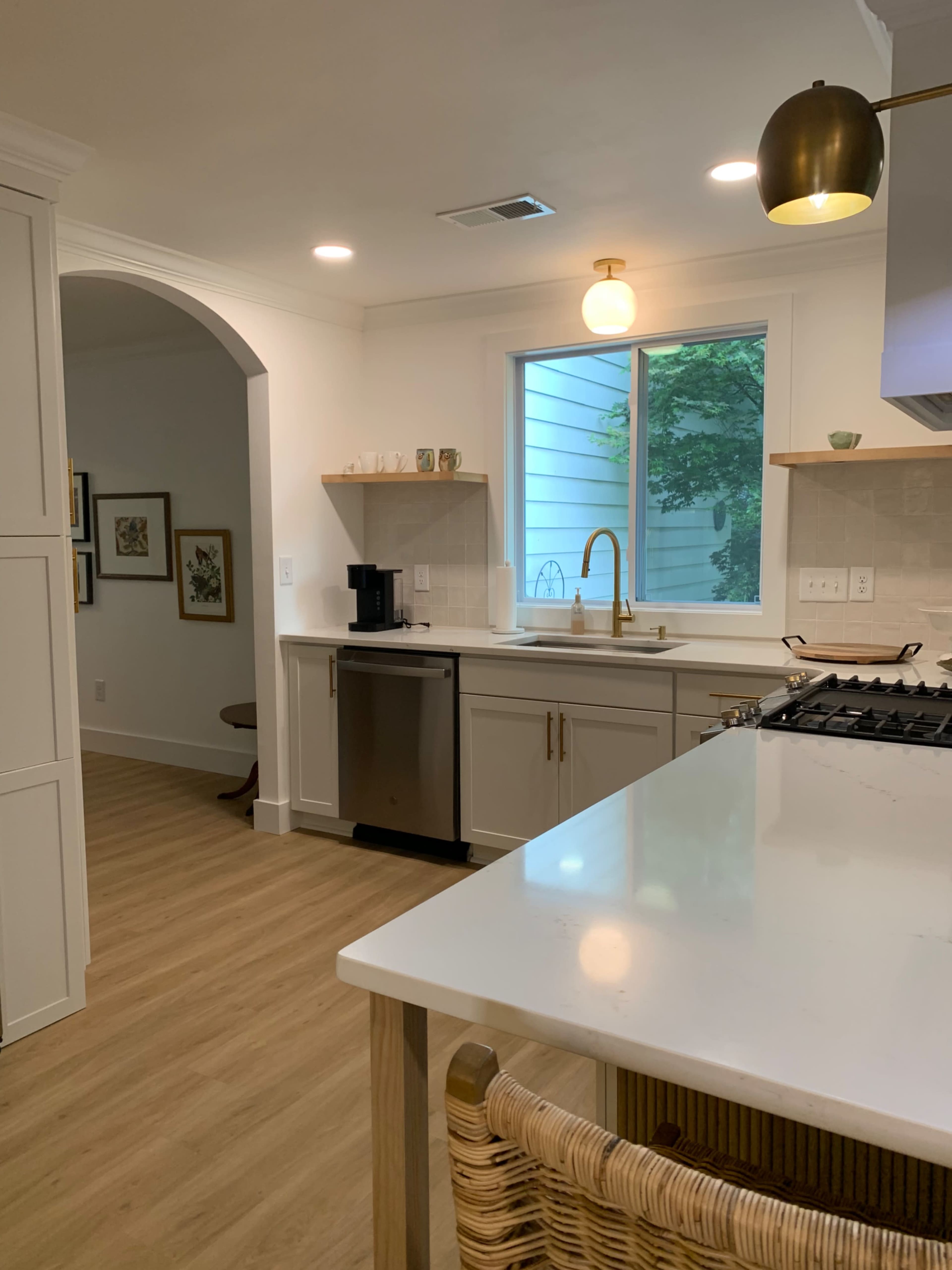 A modern kitchen features a sink with a gold faucet, an island with wooden stools, and large windows providing natural light.