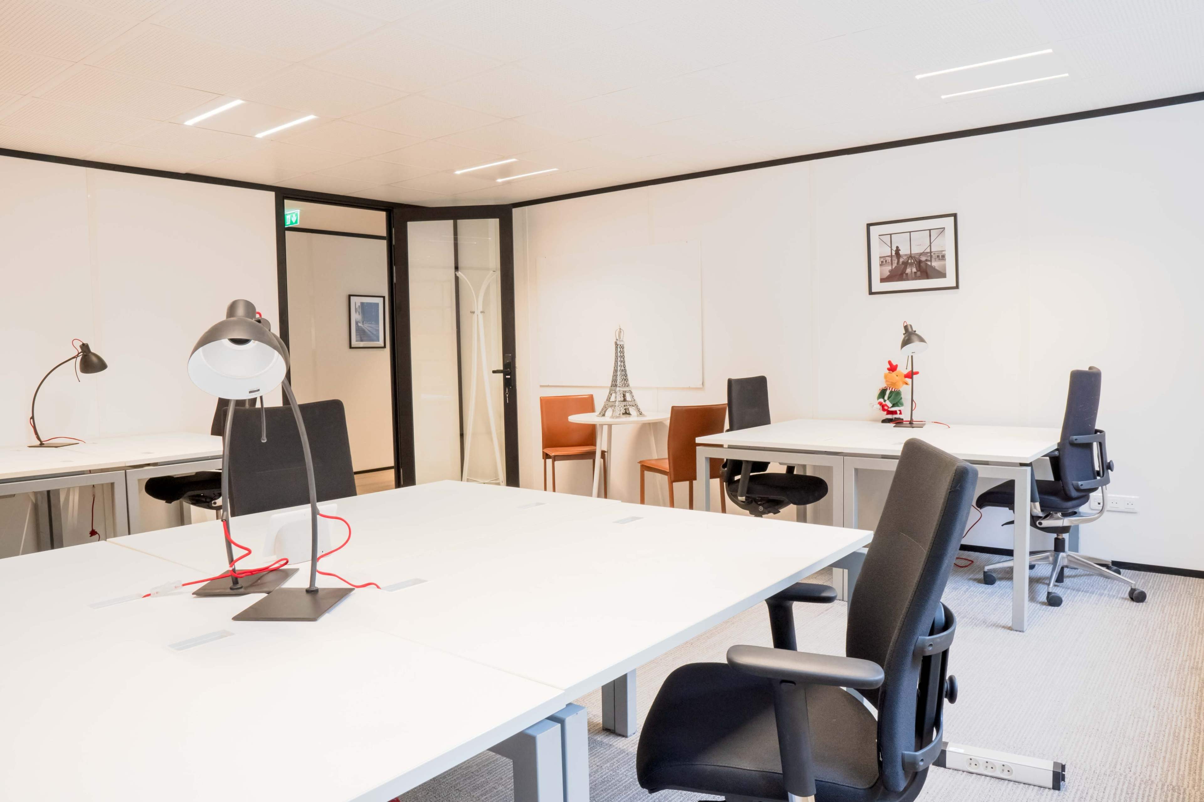 The image shows a modern office space with several desks, chairs, and a decorative Eiffel Tower figurine on one of the tables.
