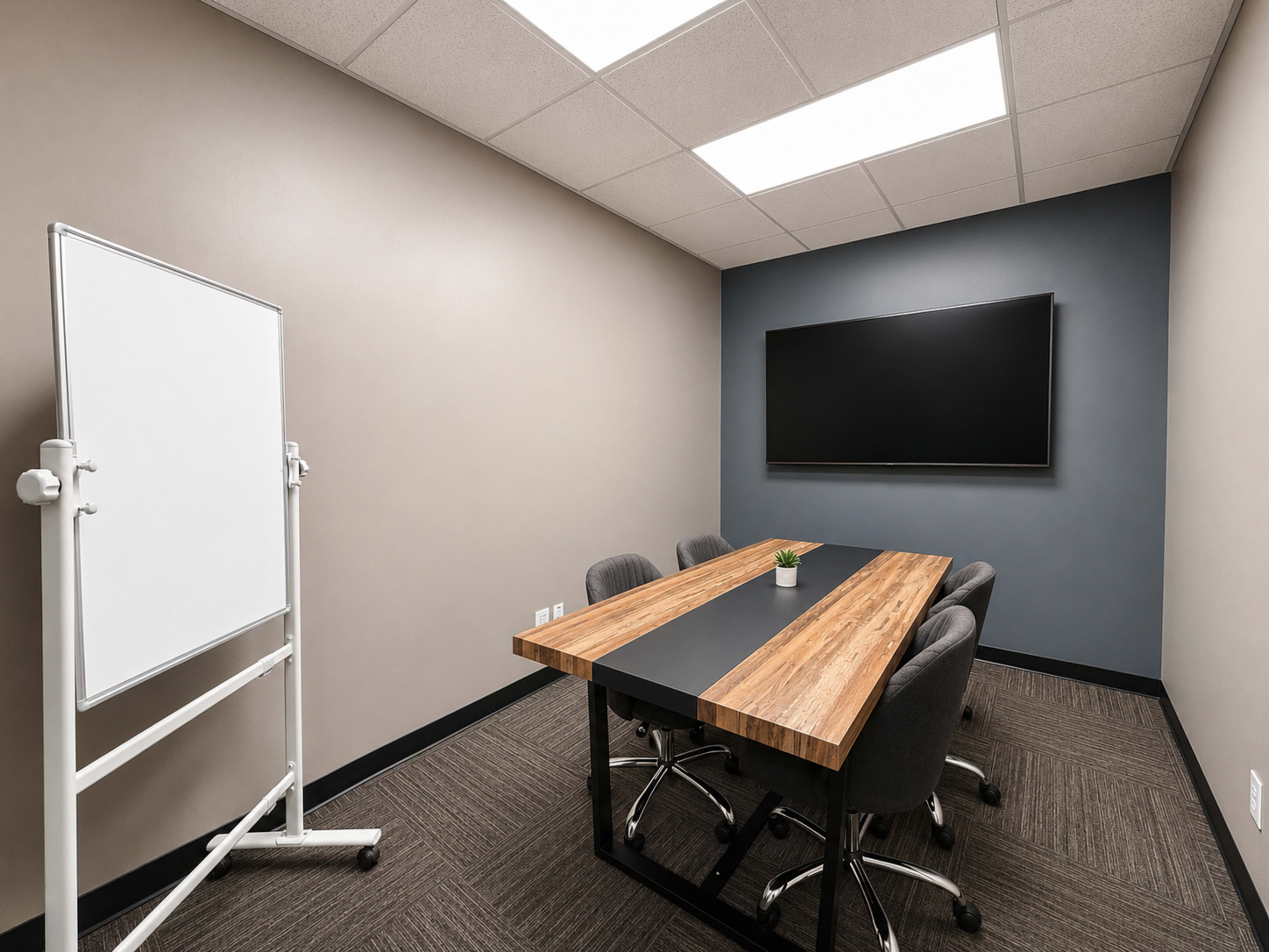 The image shows a small conference room with a wooden table, four upholstered chairs, a whiteboard, and a wall-mounted television.