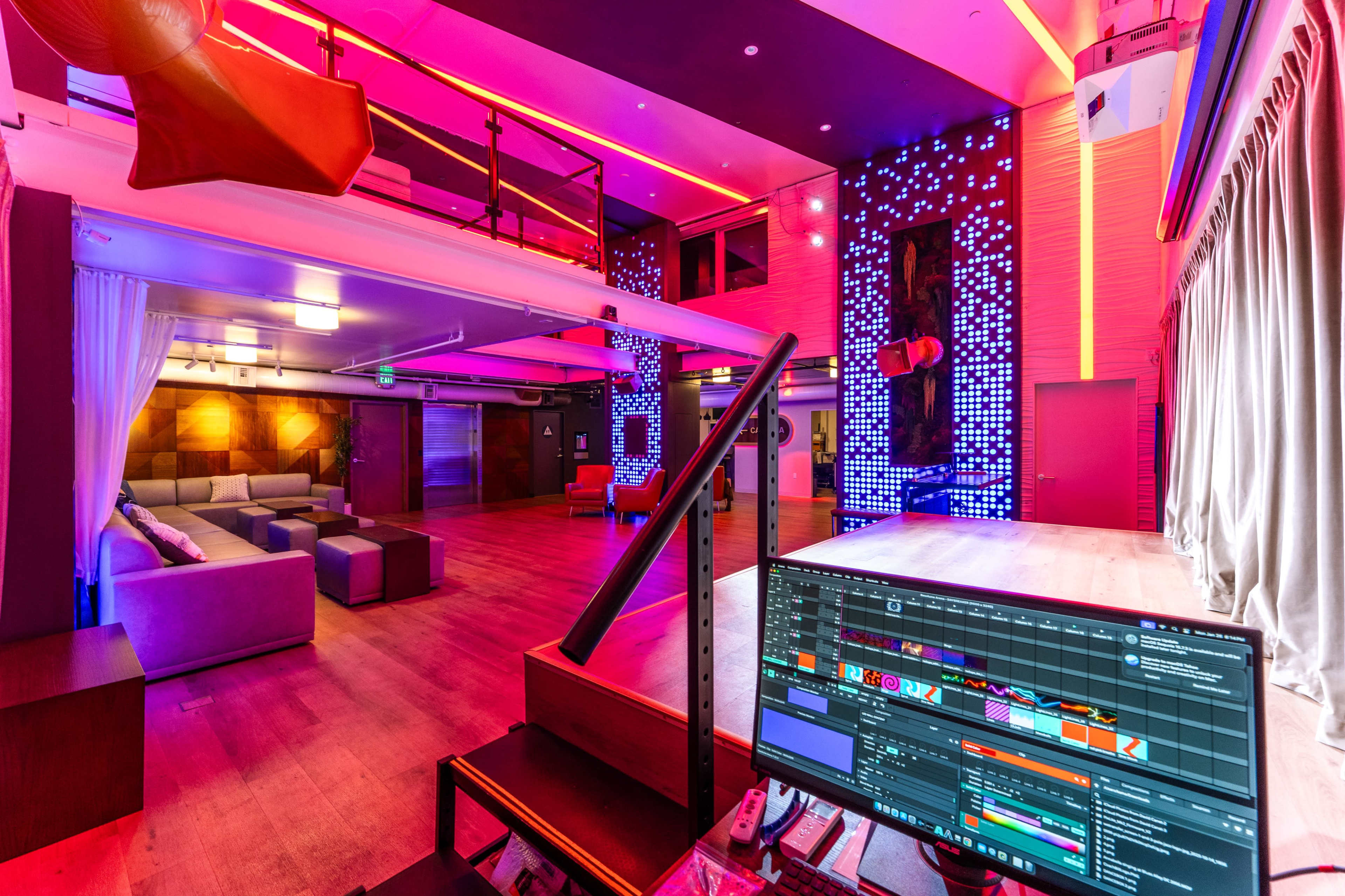 The image shows a spacious lounge area with colorful LED lighting, featuring seating arrangements and a large screen setup.