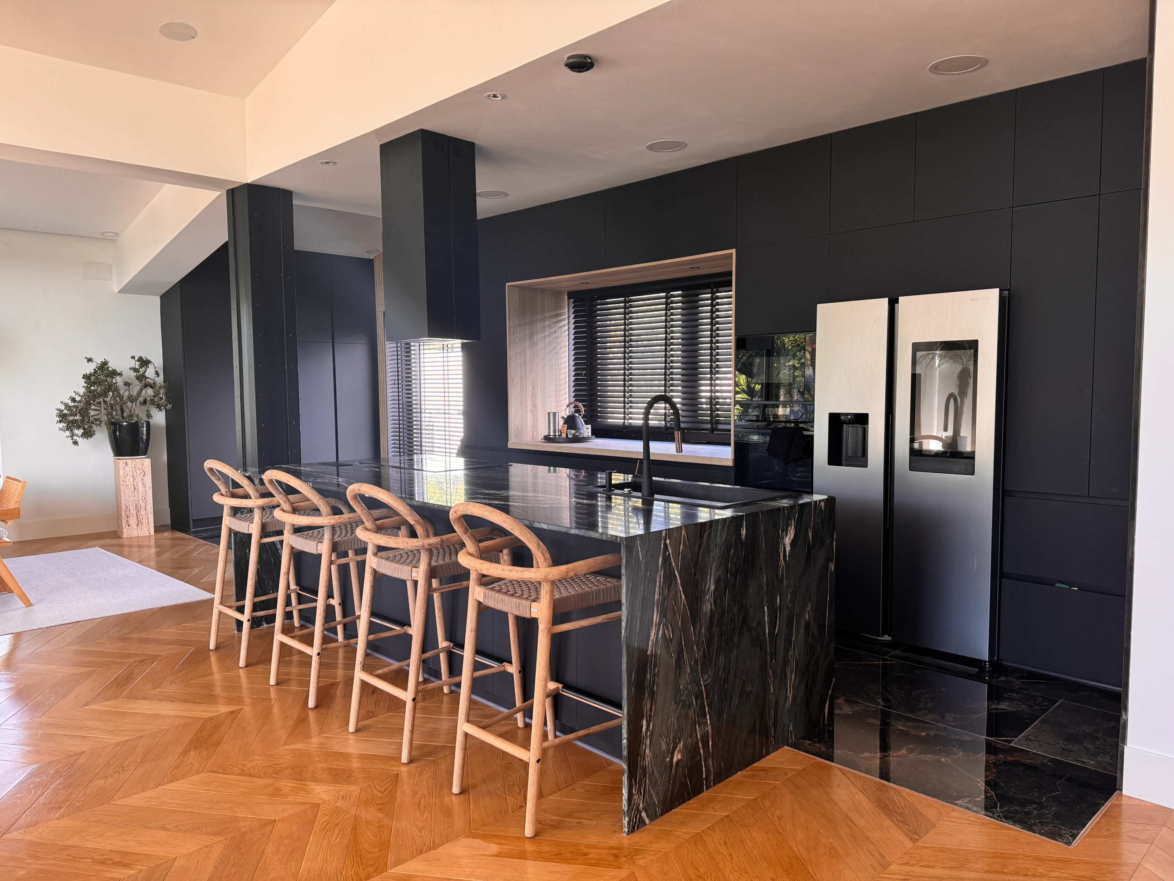 The image shows a modern kitchen featuring a large dark marble island with seating, sleek cabinetry, and stainless steel appliances.