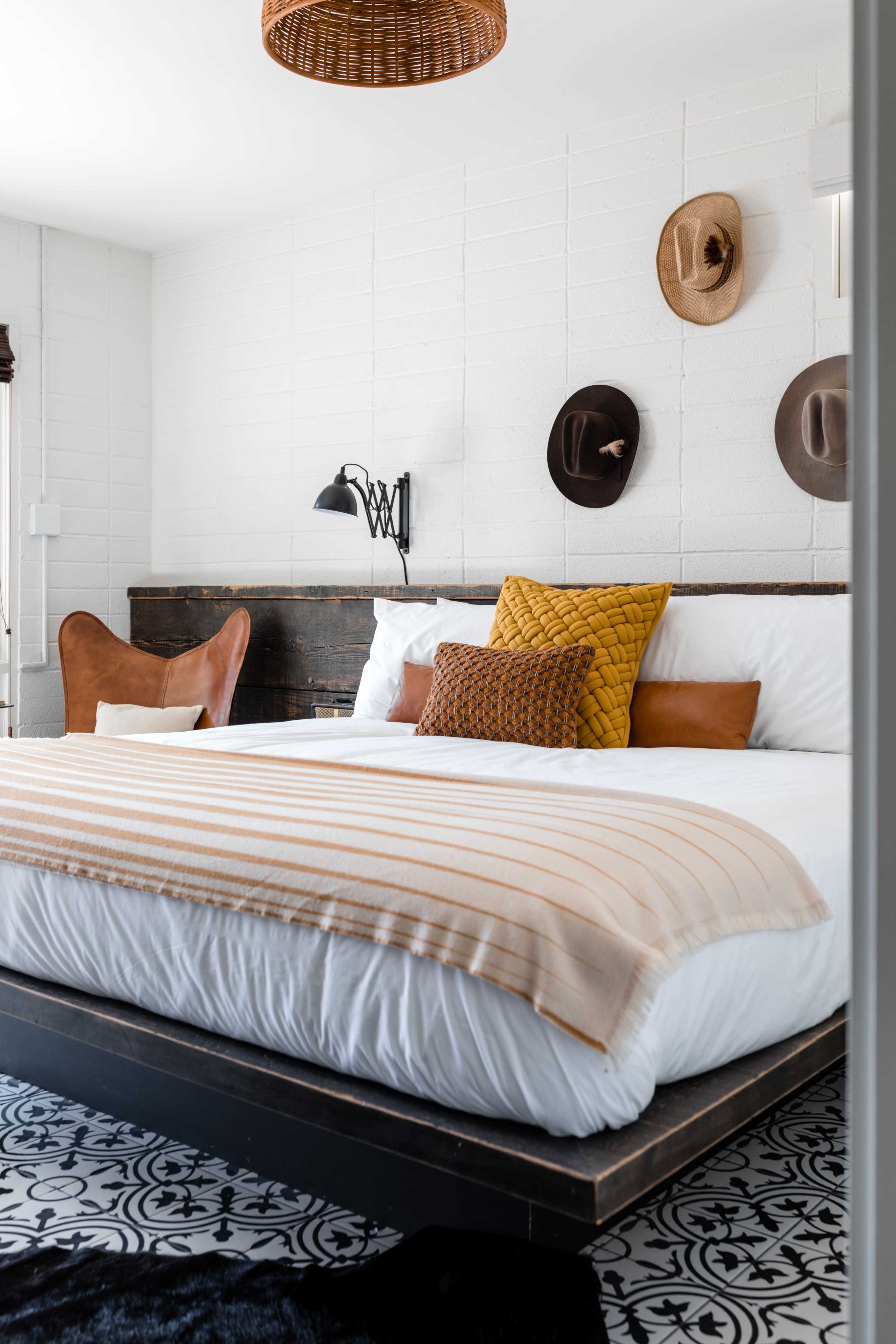 A neatly arranged bedroom features a large bed with decorative pillows, a woven throw blanket, and hats displayed on the wall.