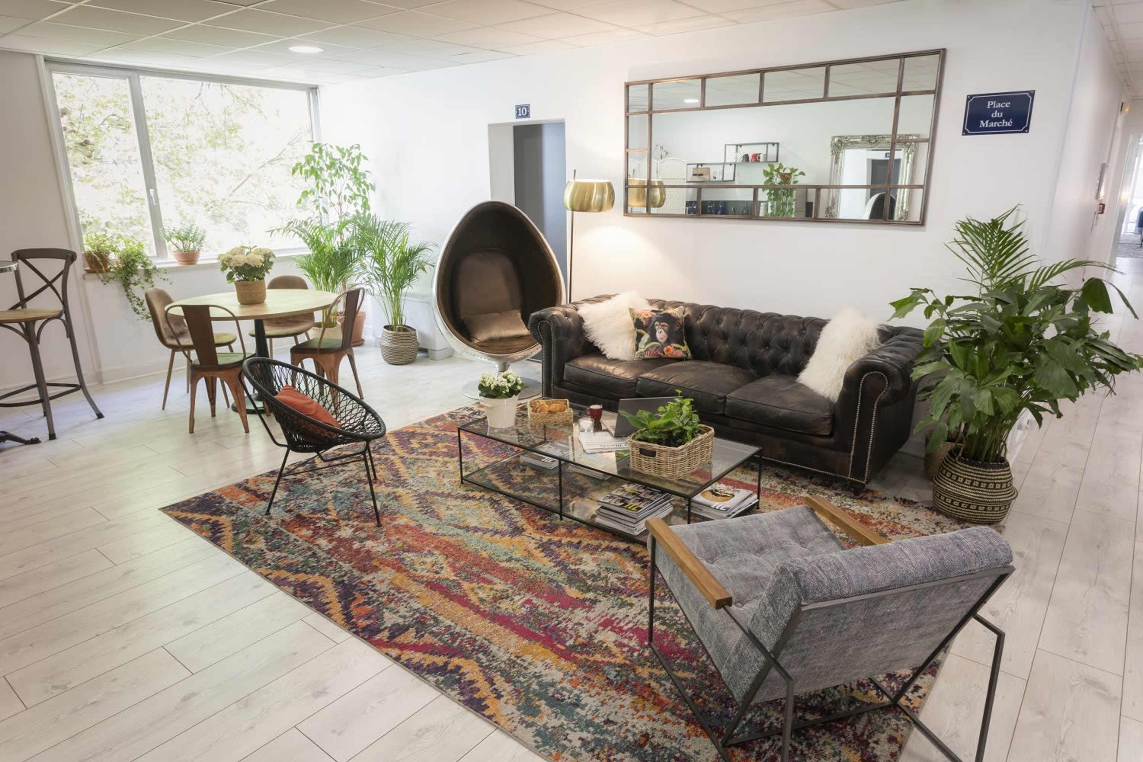 A cozy lounge area features a black leather sofa, a glass coffee table with plants, and various seating arrangements around a colorful rug.