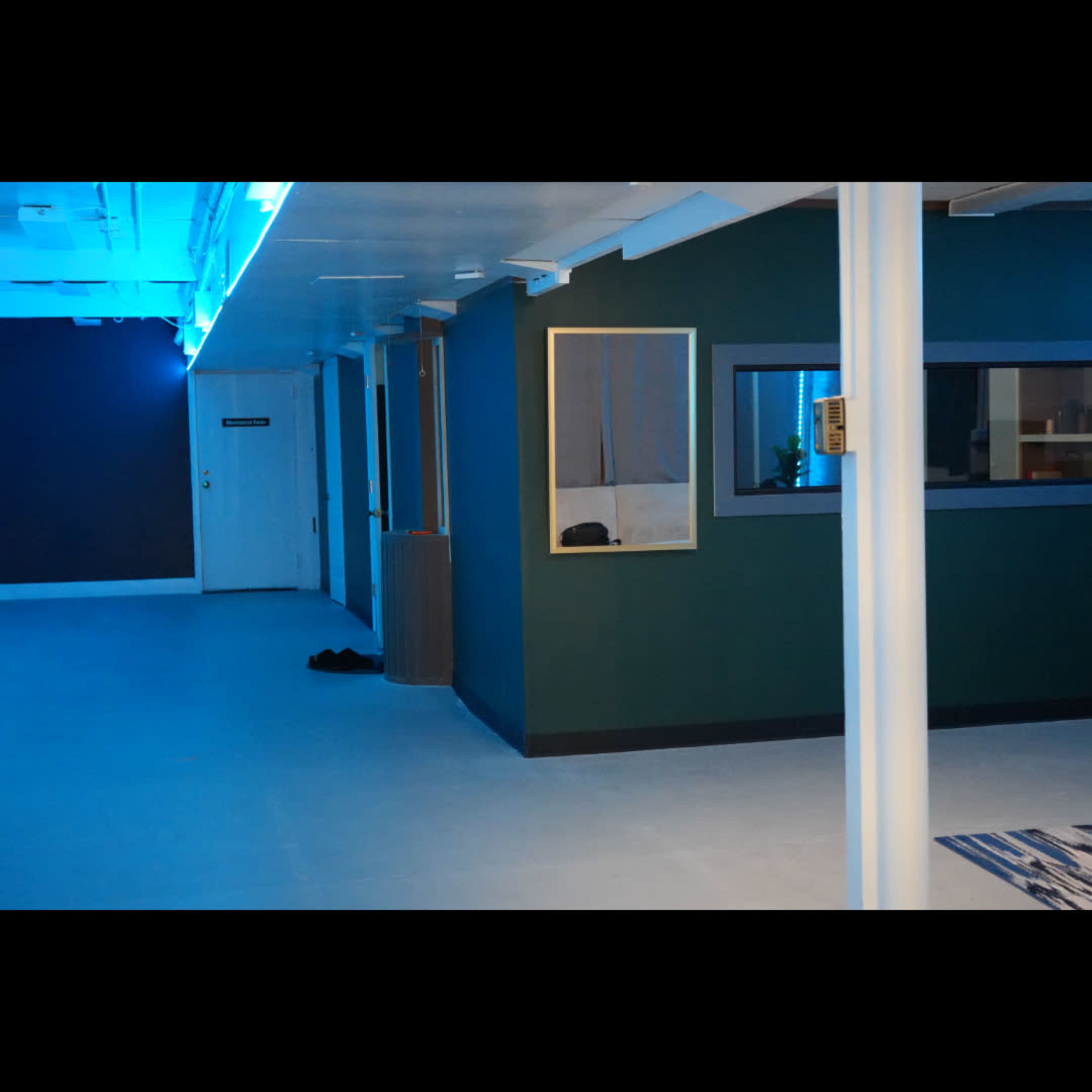 The image shows an interior room with blue lighting, a green wall, a large mirror, and a door at the far end.