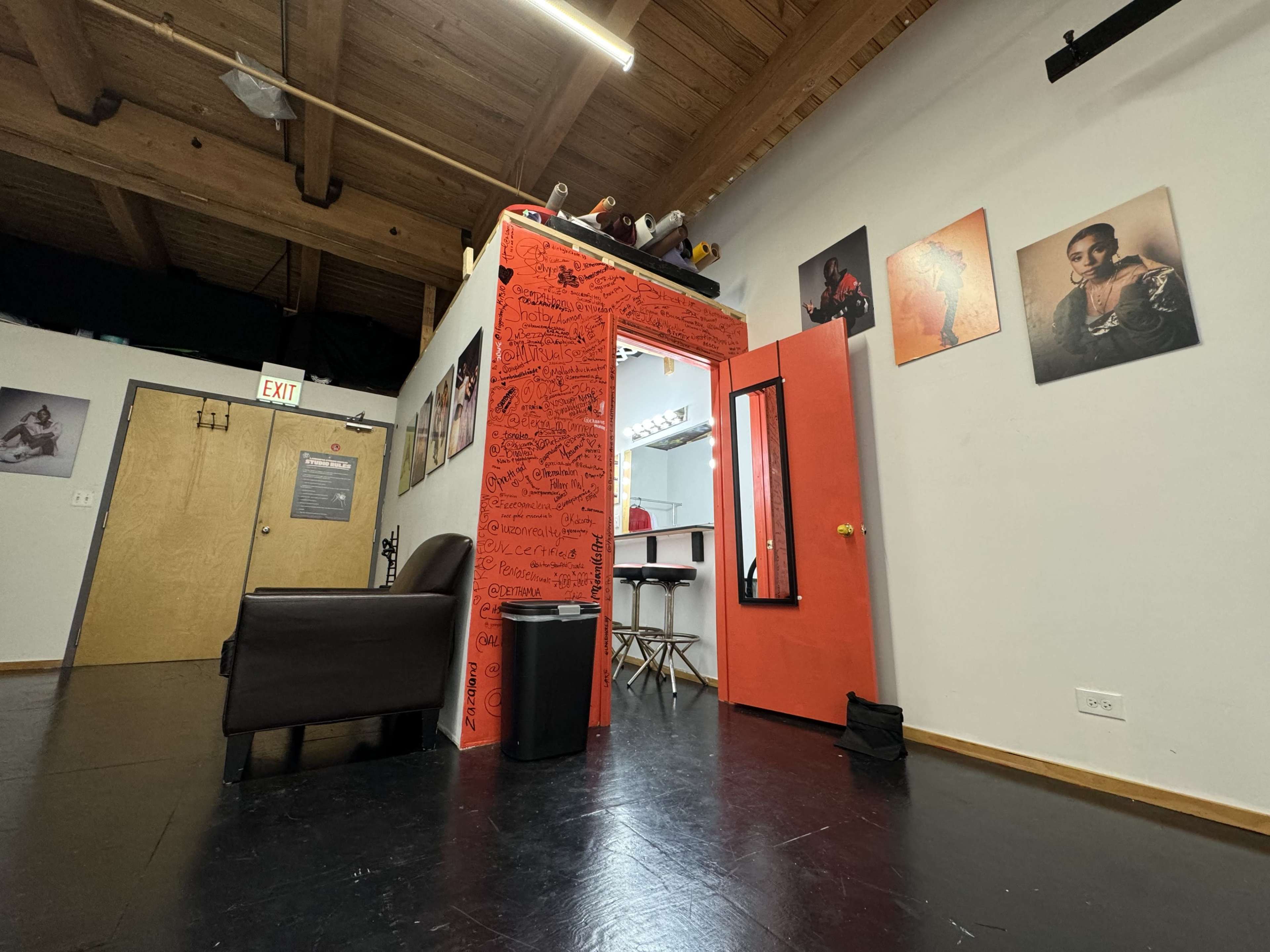 A vibrant studio space featuring a bright orange doorway, a brown couch, and various framed photographs on the walls.