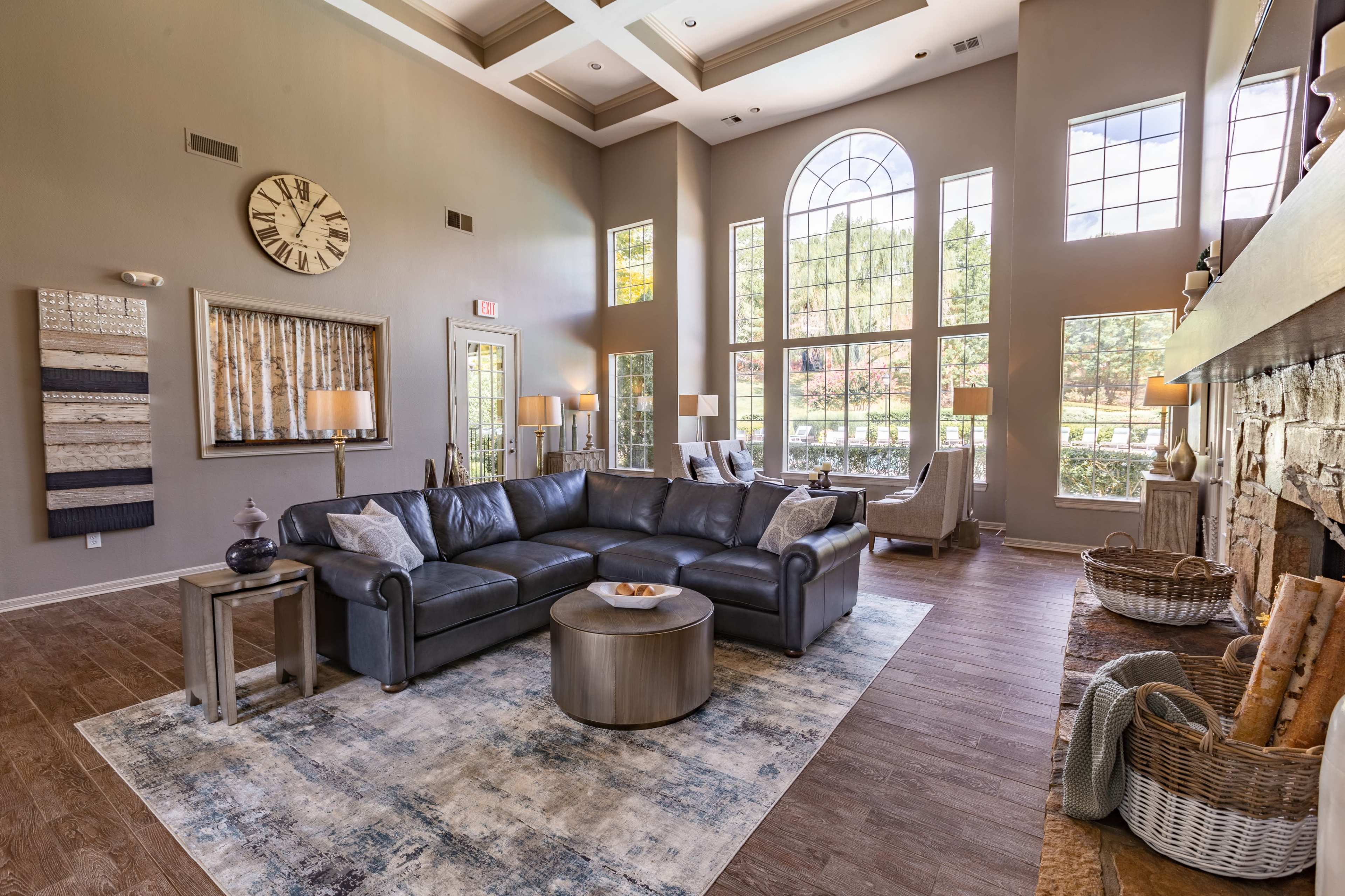 The image shows a spacious living room with large windows, a sectional sofa, a round side table, and a decorative rug.