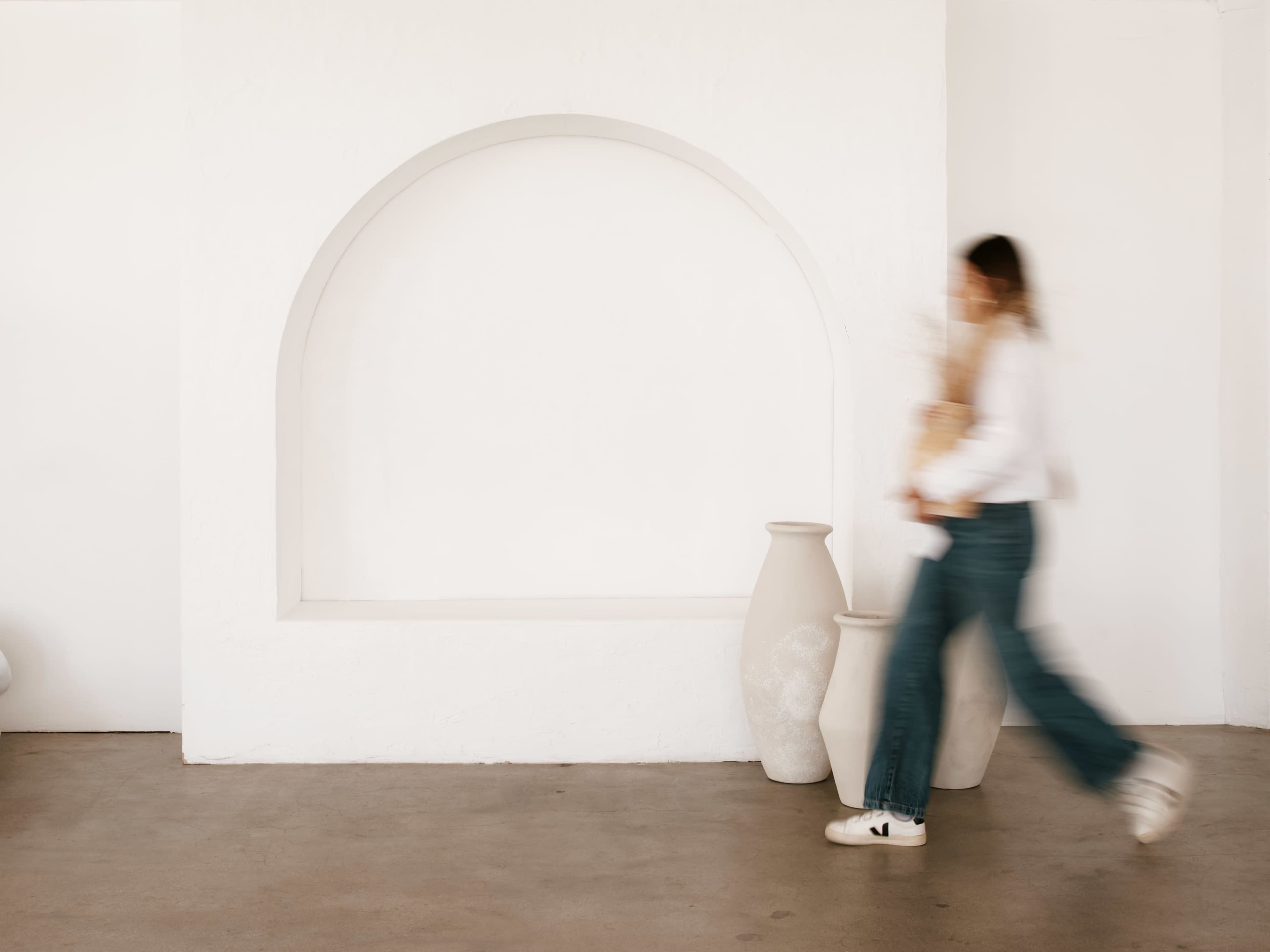A person walks past two large ceramic vases in a minimalist white interior.