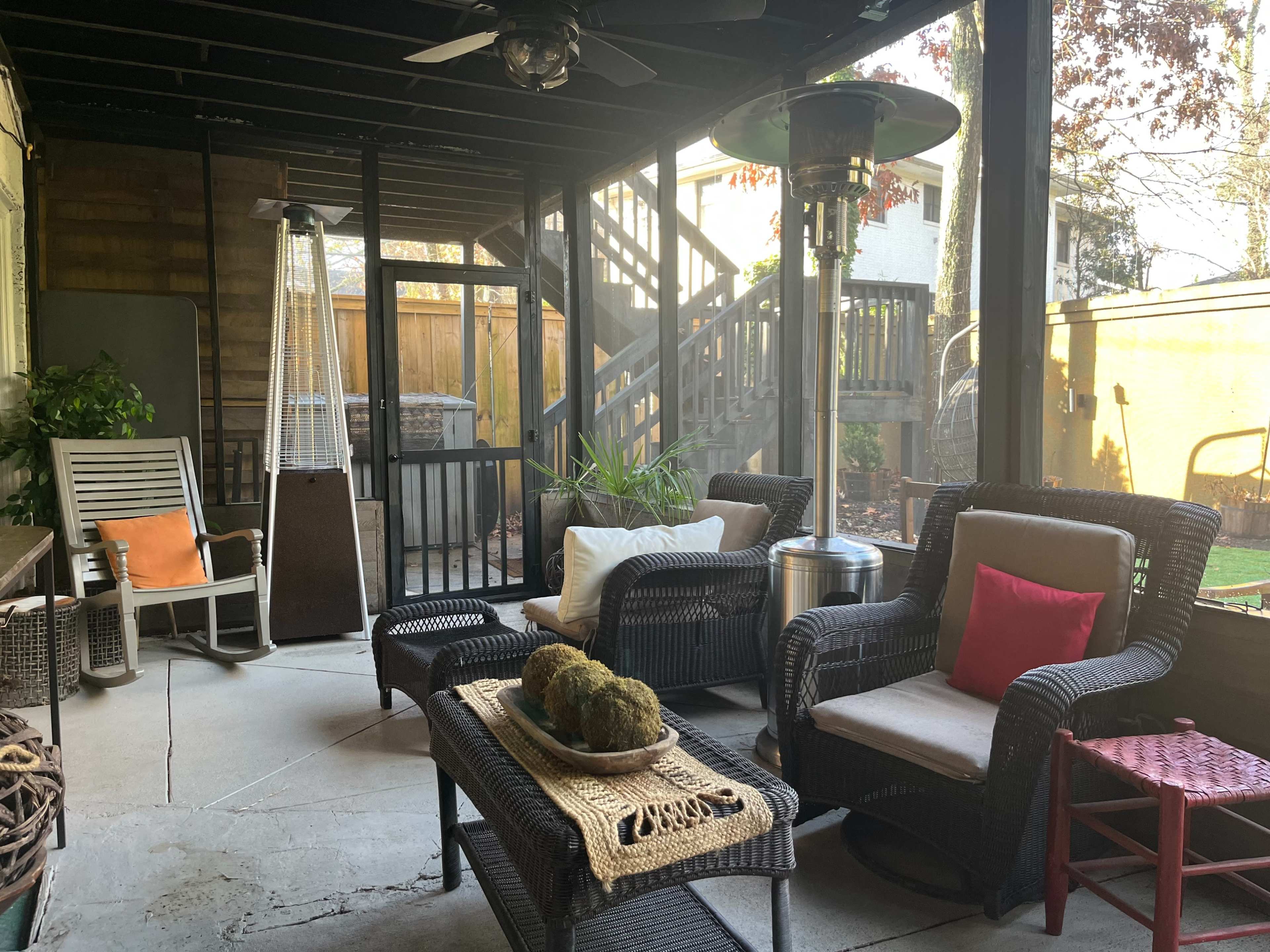 A covered patio area with wicker furniture, a heating lamp, and steps leading to a higher level.