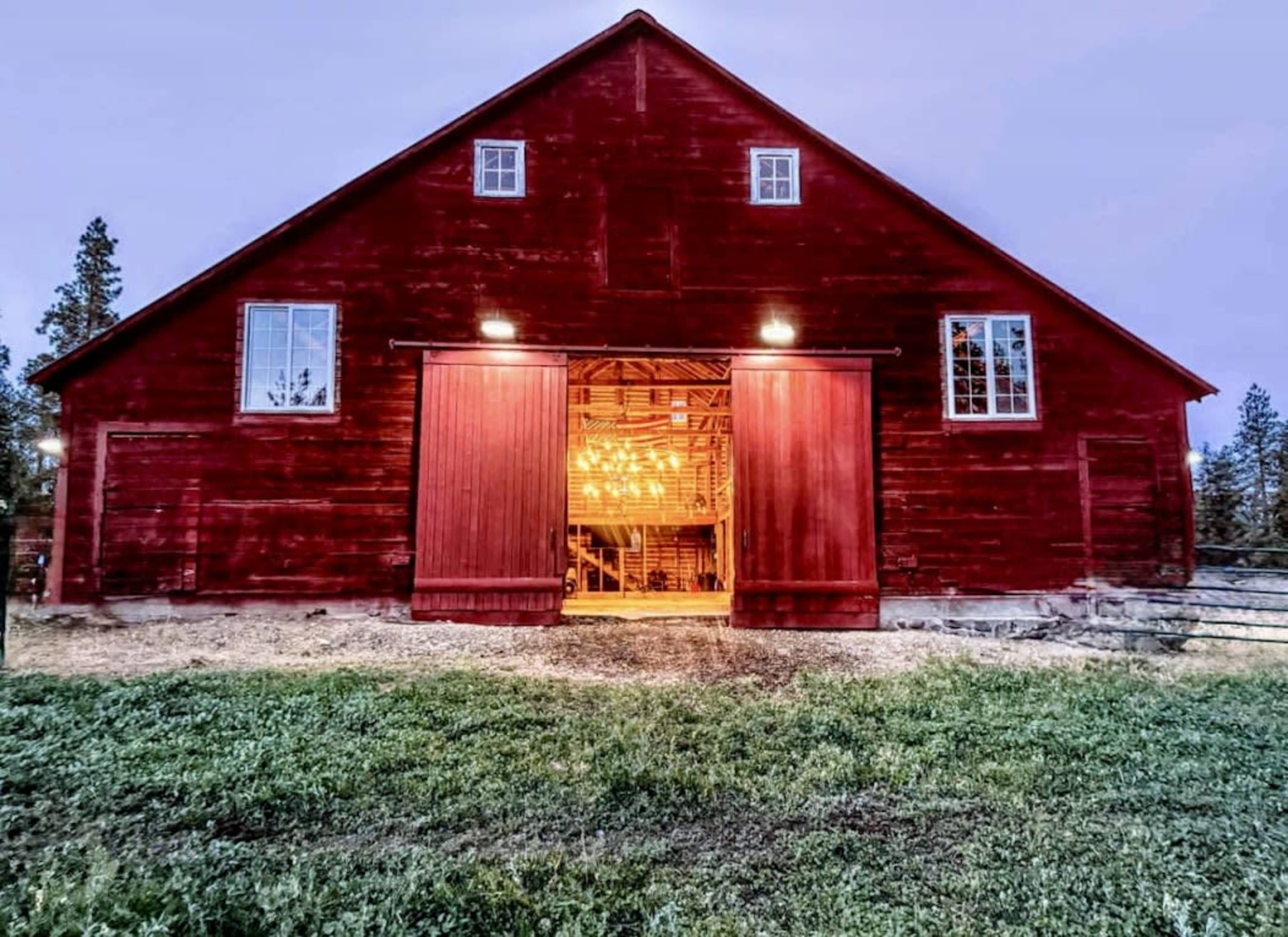 A red barn with open doors is illuminated from within, set against a twilight sky.