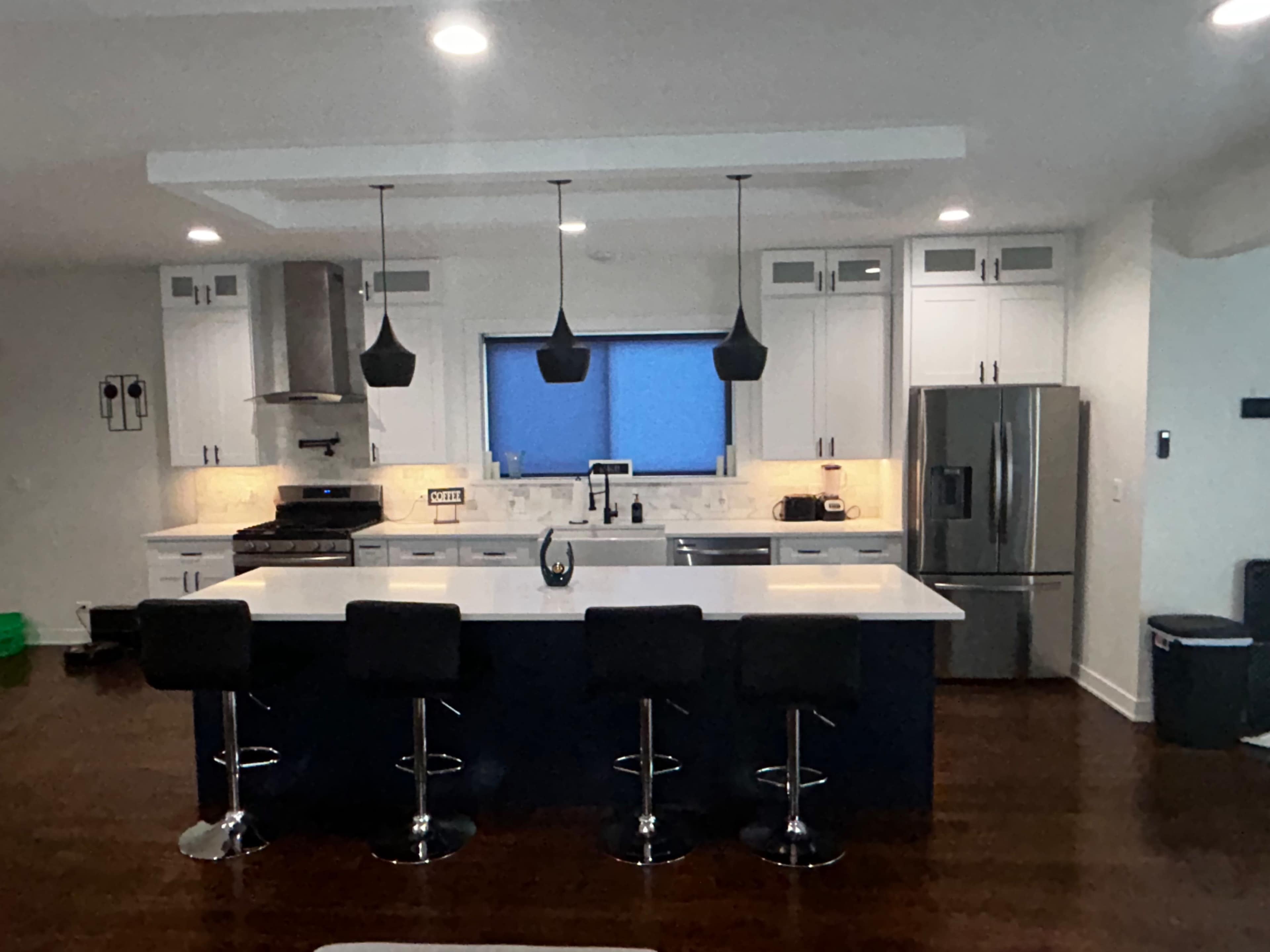 The image shows a modern kitchen with white cabinetry, a large island with bar stools, and stainless steel appliances.