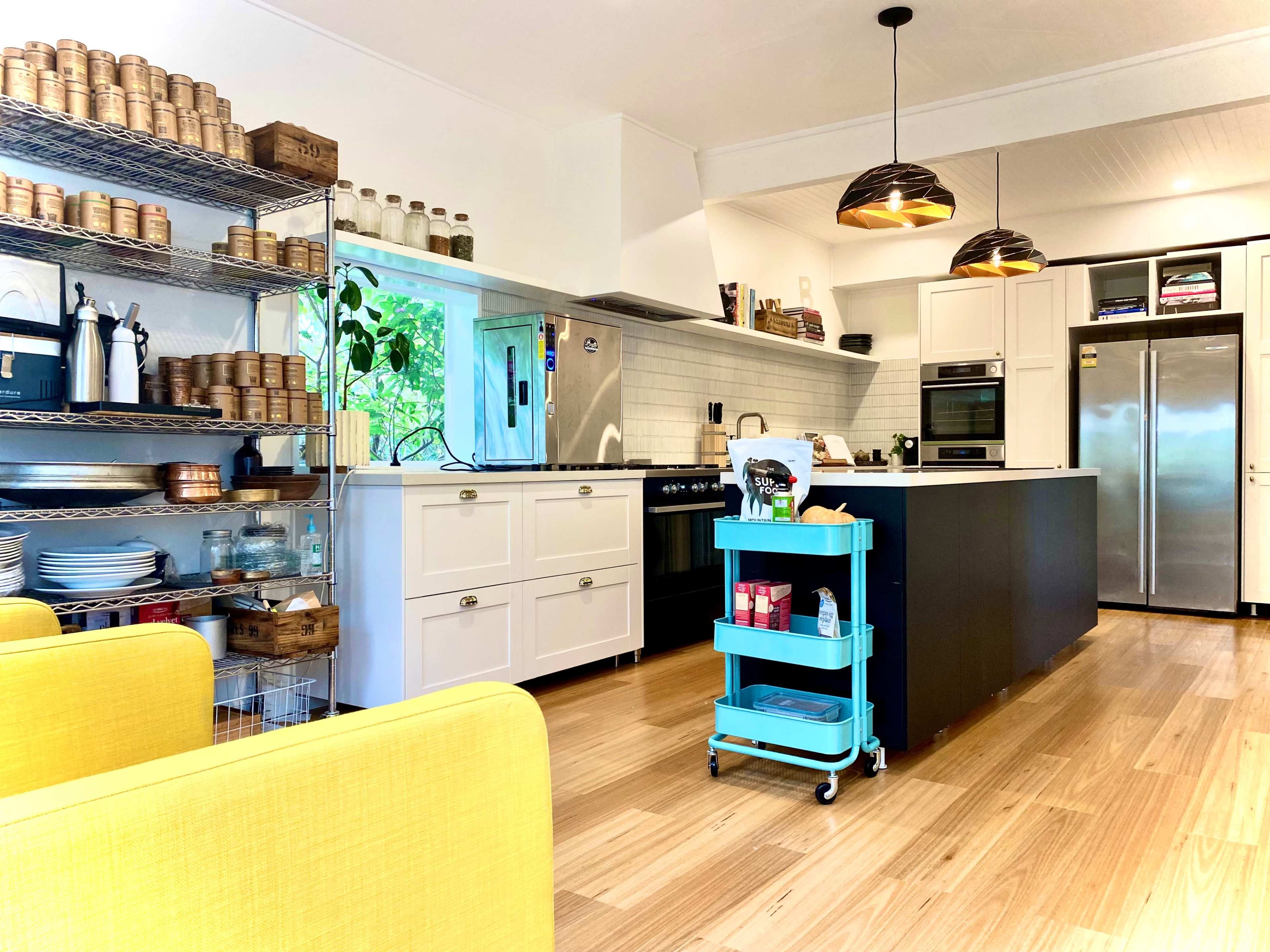 A modern kitchen with a central island, stainless steel appliances, and open shelving holding various kitchenware and storage containers.