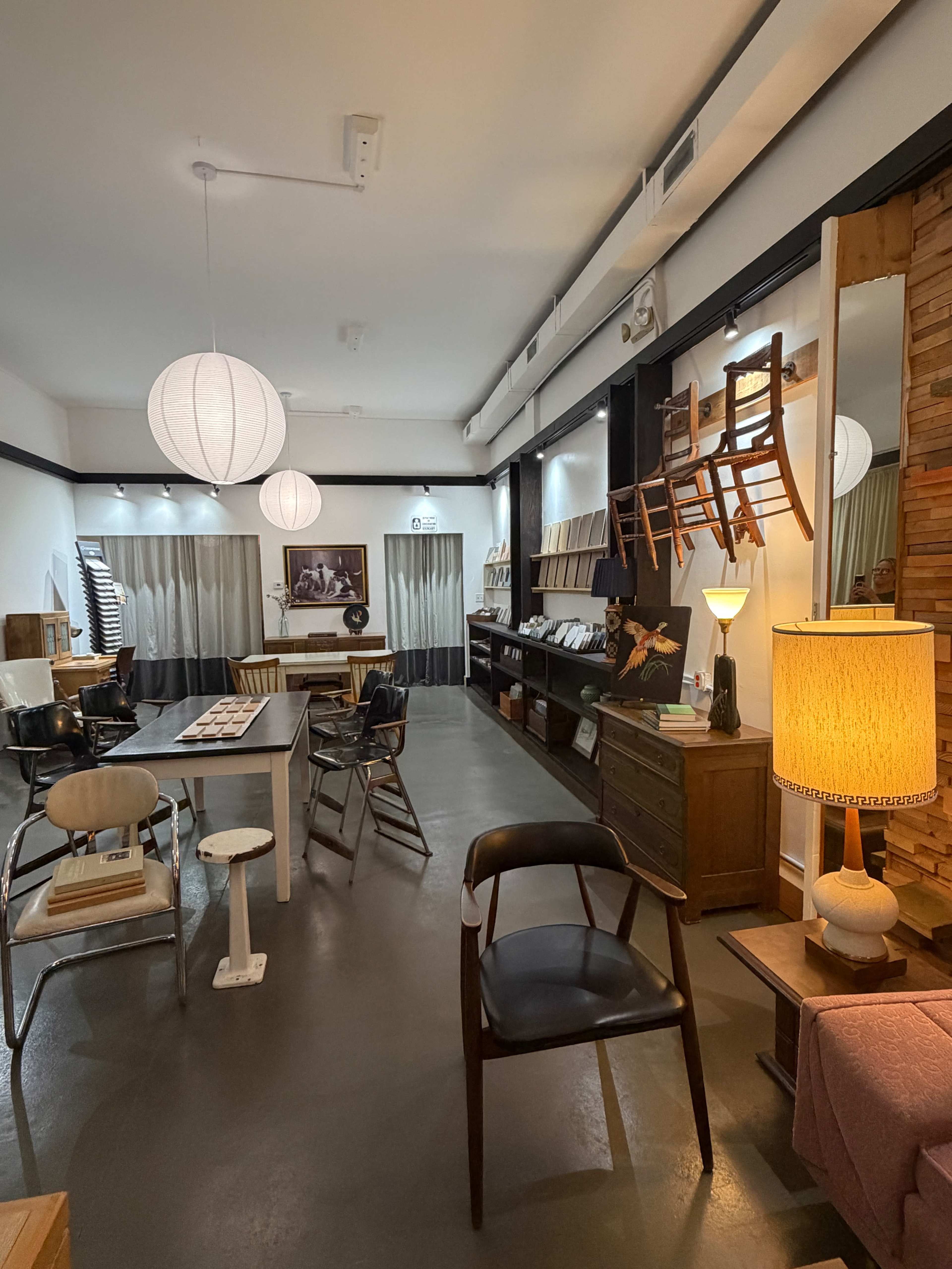 The image shows a modern interior space with a combination of seating, tables, and decorative elements, featuring warm lighting and wooden accents.