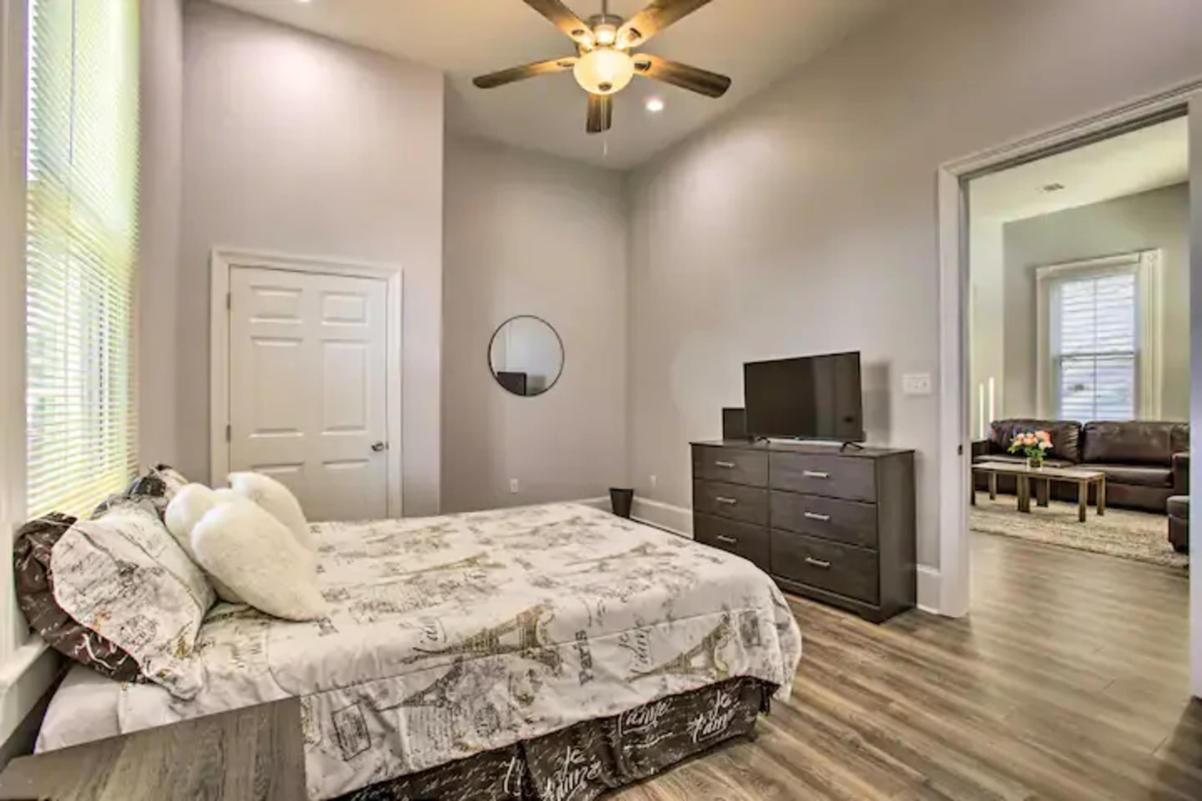 A bedroom with a bed, dresser, television, and a door leading to another room.