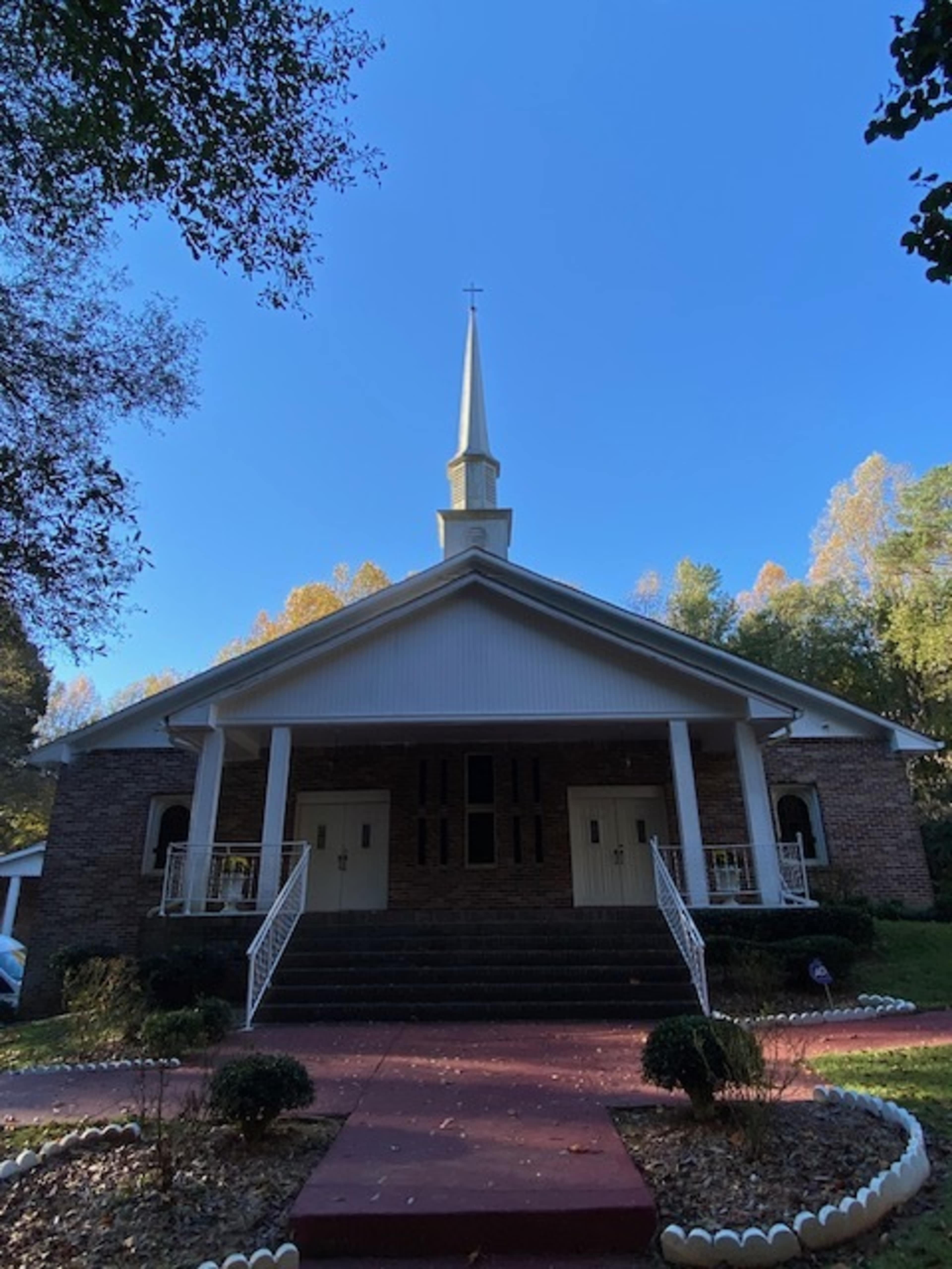The image shows a church building with a tall steeple and a set of stairs leading to its entrance, surrounded by trees and a clear blue sky.