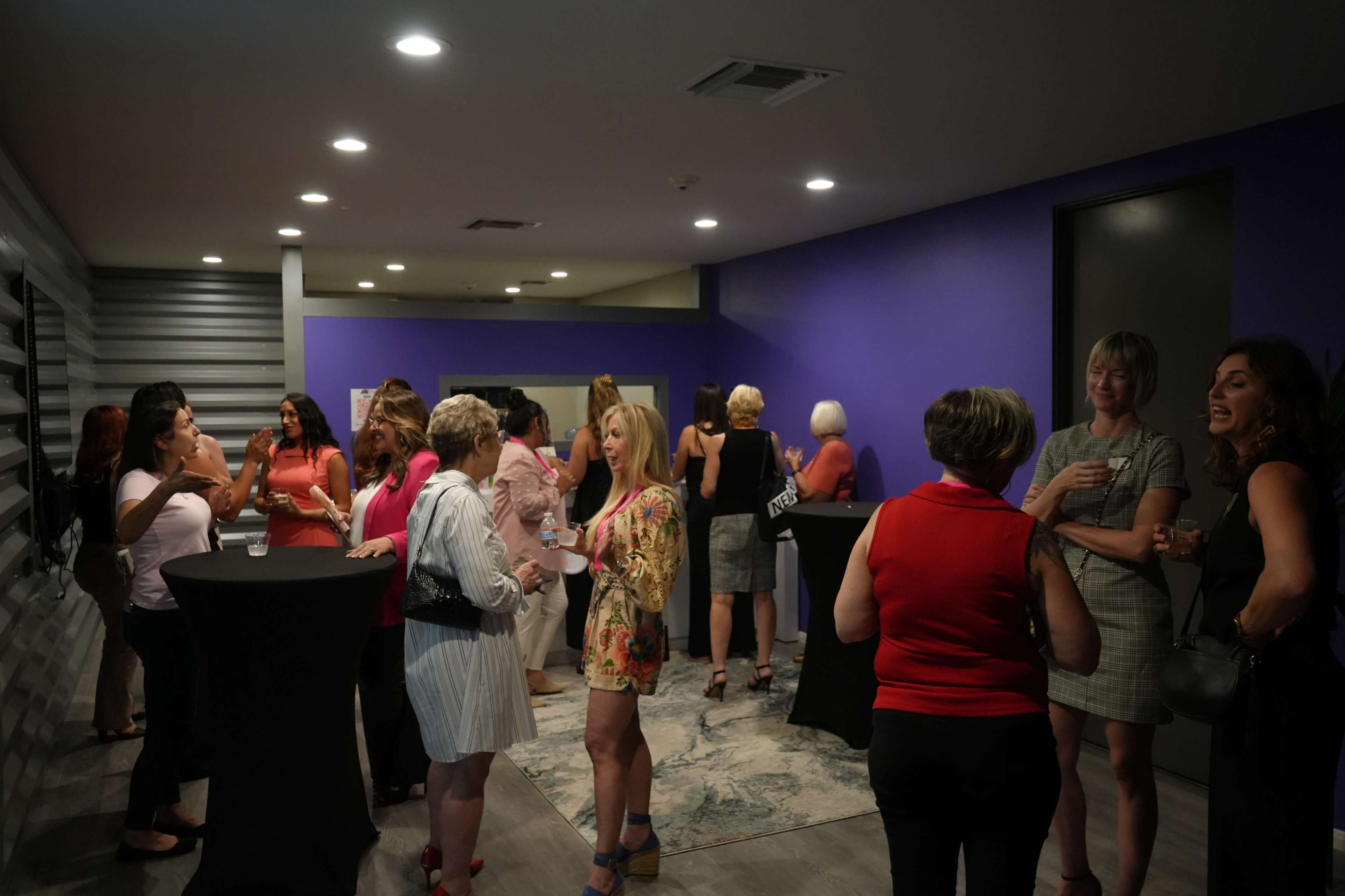 A group of individuals socializes in a well-lit room with purple walls and modern decor.