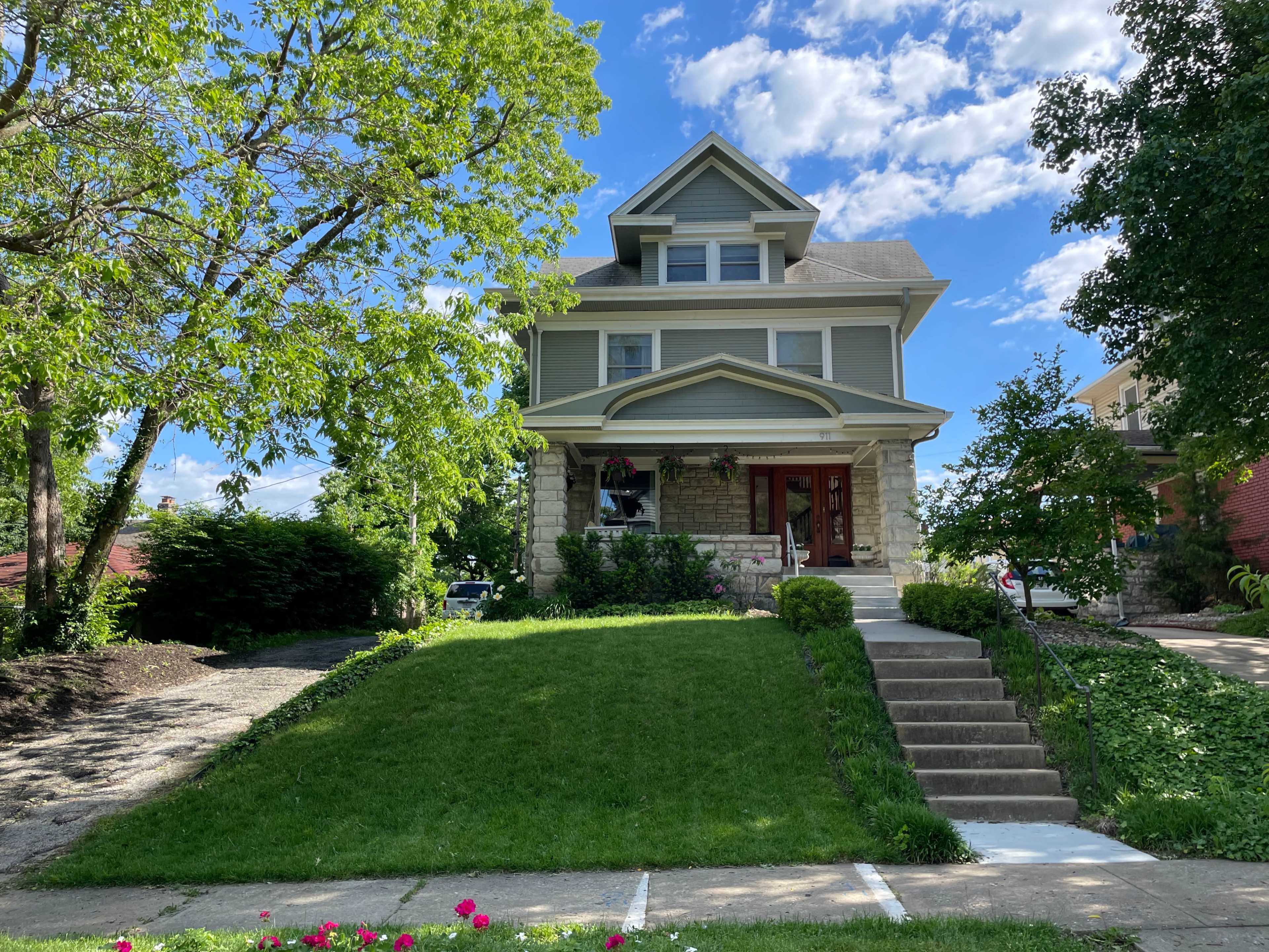 A three-story house with a stone and siding facade is set on a lush green lawn with steps leading up to the entrance.