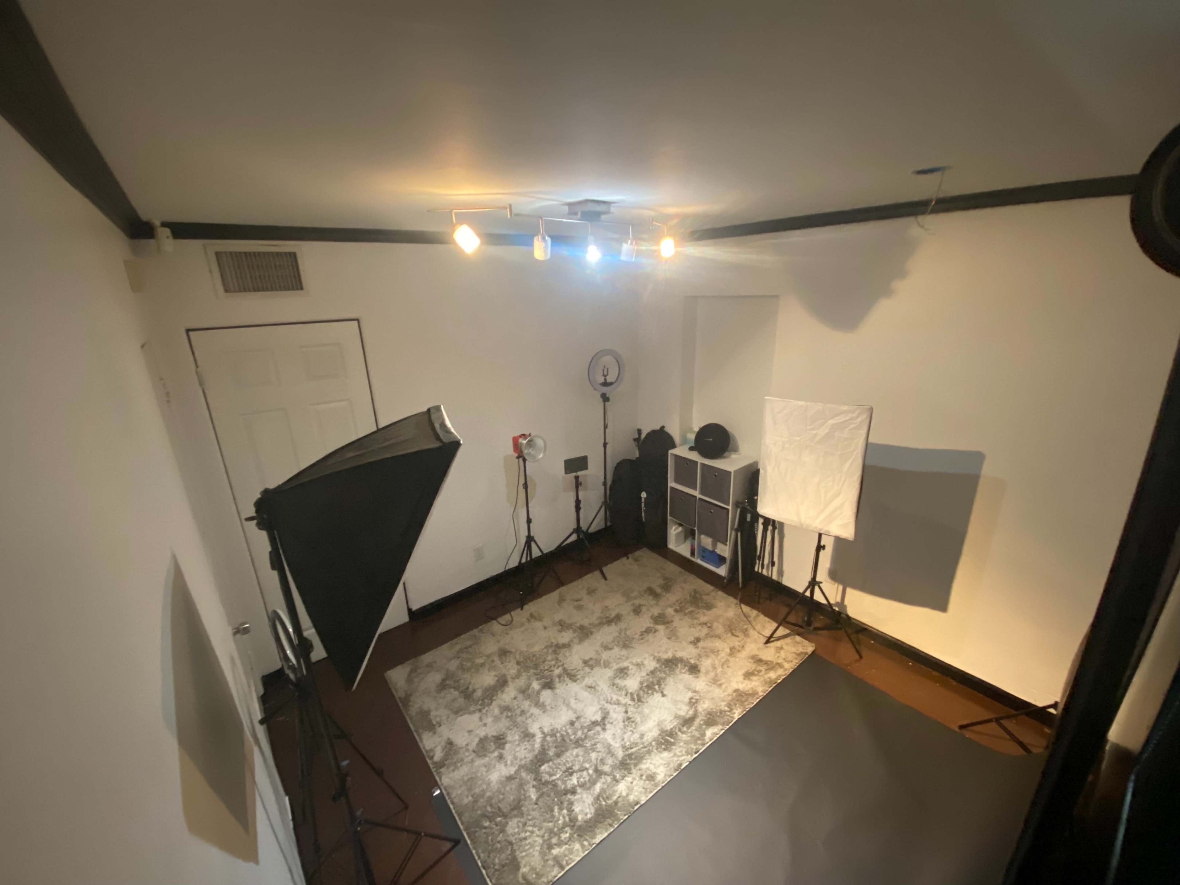 A photography or videography studio featuring two light stands, a rug, a backdrop, and various equipment organized in a corner.
