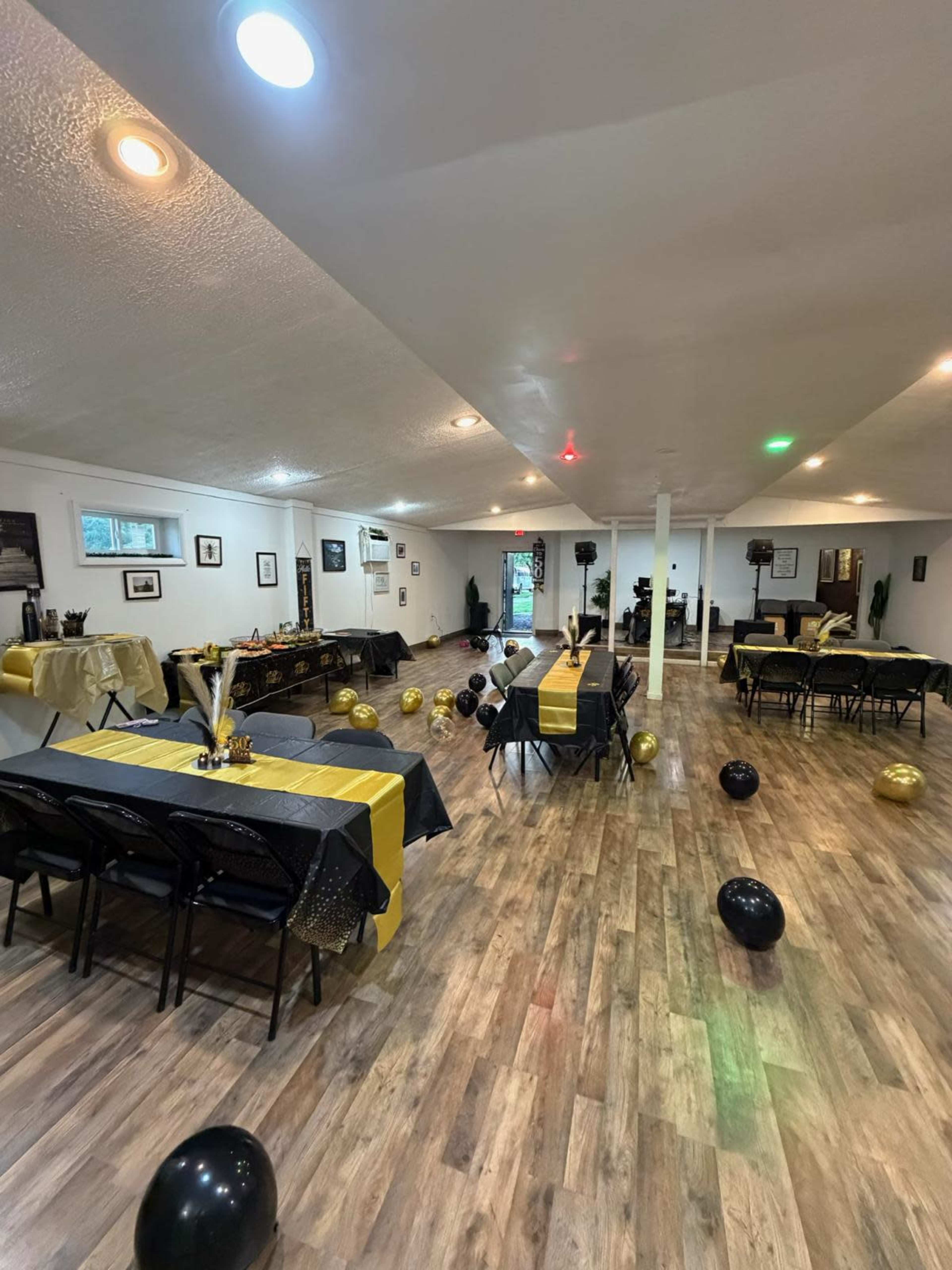 A spacious event room is set up with black and gold decorations, tables, and scattered balloons.