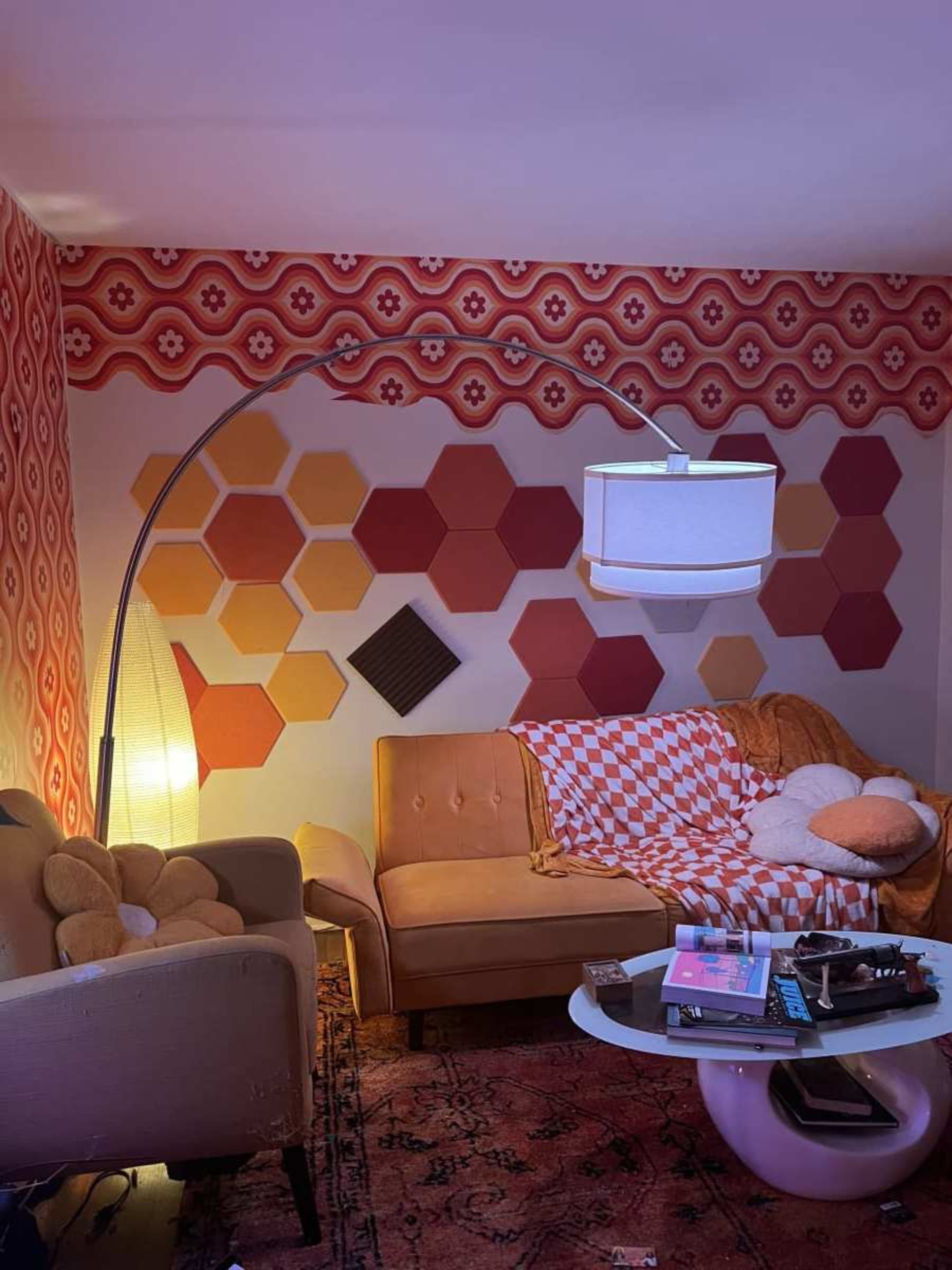 The room features a retro-inspired design with hexagonal wall panels, a curved floor lamp, and a beige couch adorned with patterned cushions.