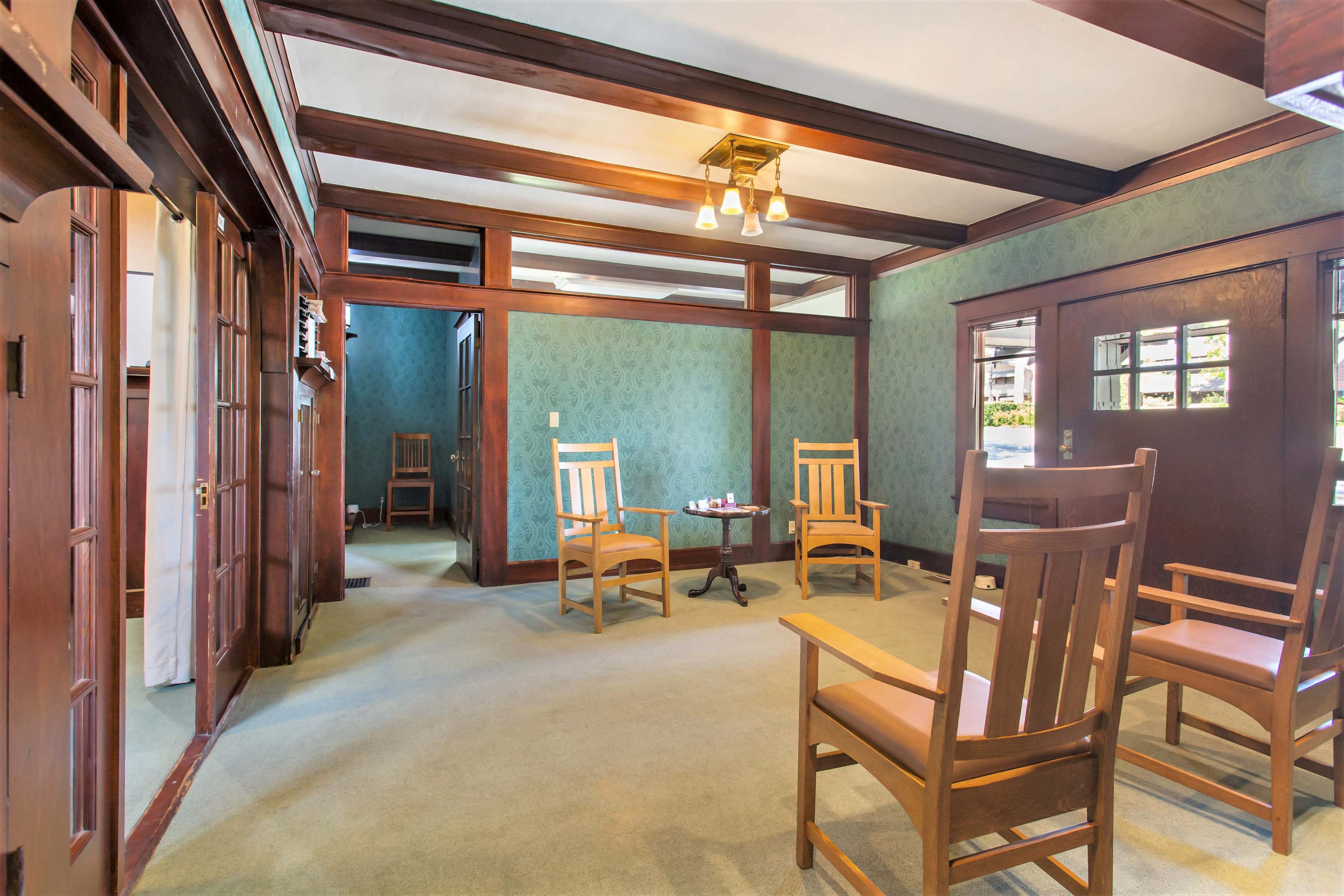 A room with wooden beams, green wallpaper, and four chairs arranged around a small table.