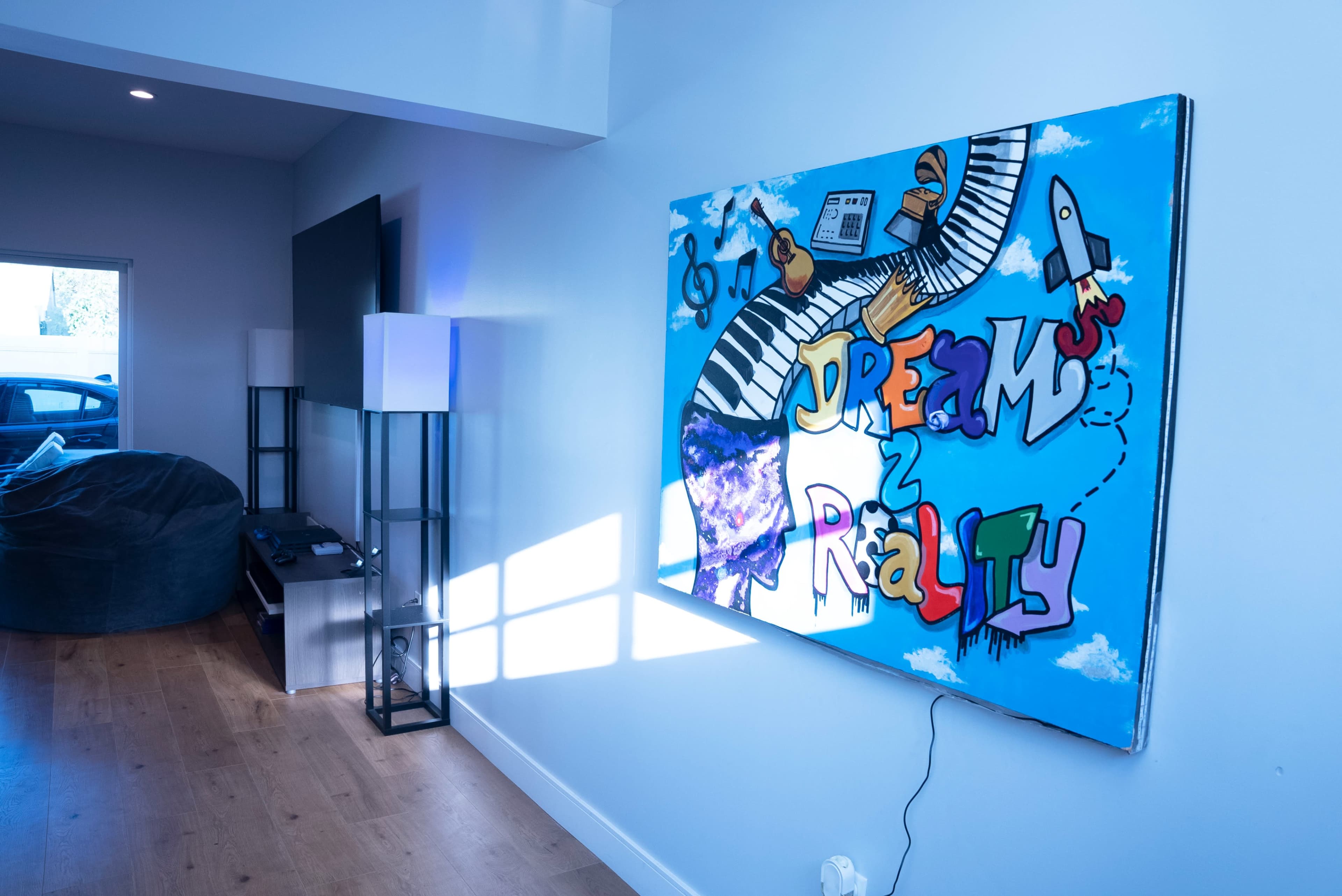 A modern living space with a colorful mural titled "Dreams 2 Reality" on the wall, featuring musical elements and a rocket, alongside a bean bag and minimalist furniture.