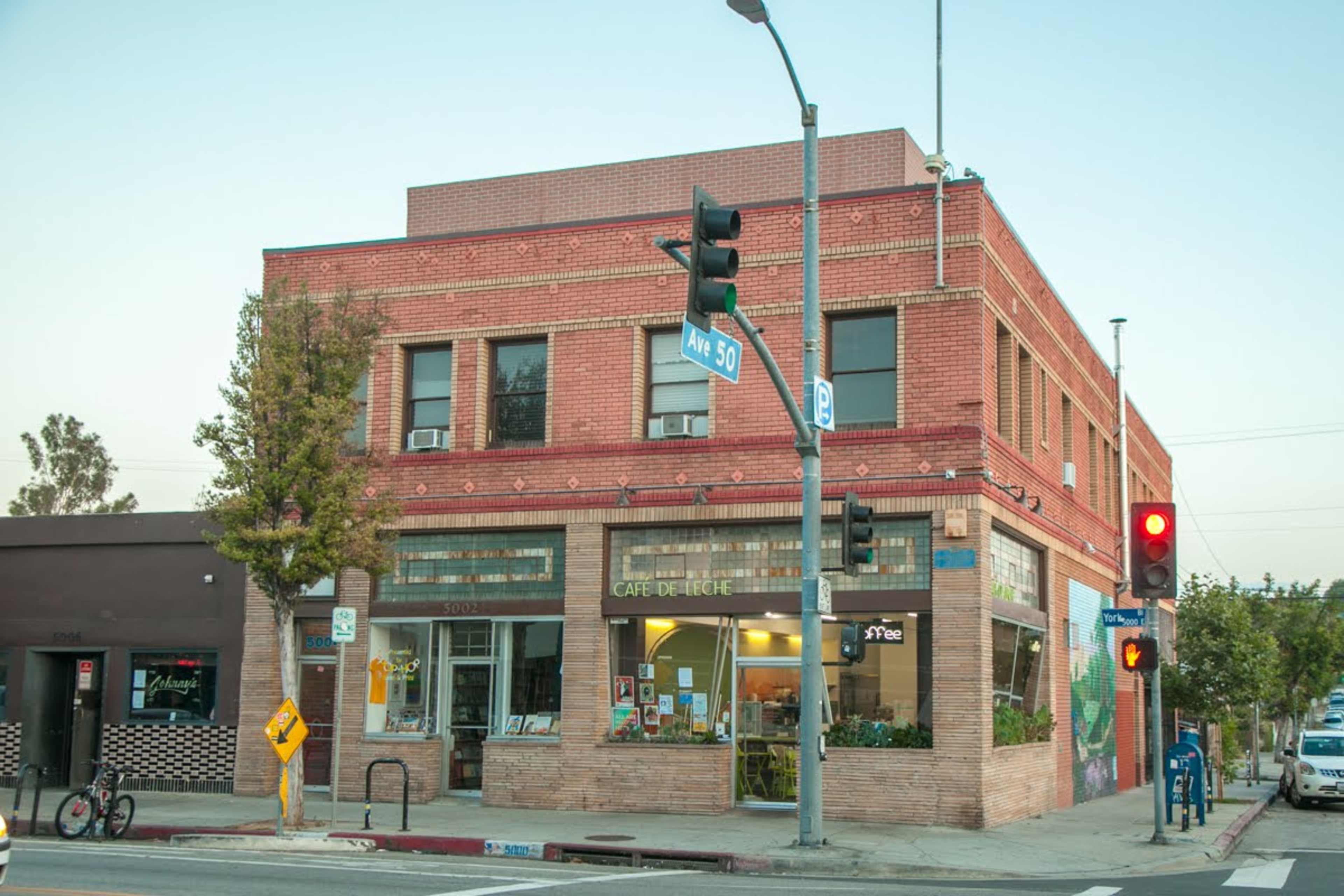 A brick building featuring a café called "Café de Linge" at a street corner with traffic lights and nearby trees.